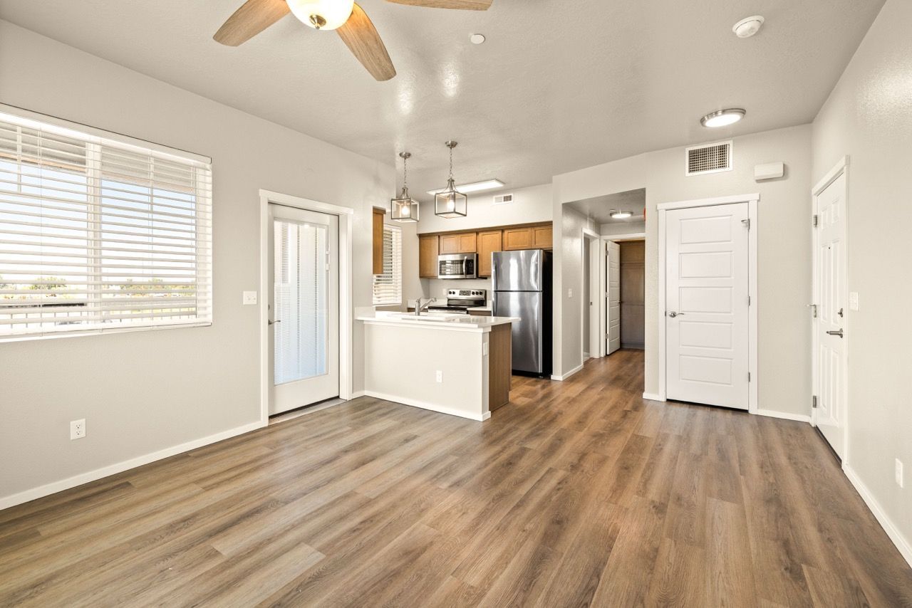 Open-concept apartment interior with kitchen island, stainless steel appliances, and window blinds.
