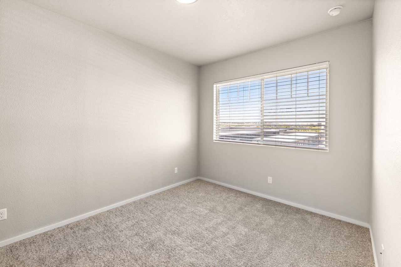 Empty neutral-toned bedroom with carpet, window and blinds.