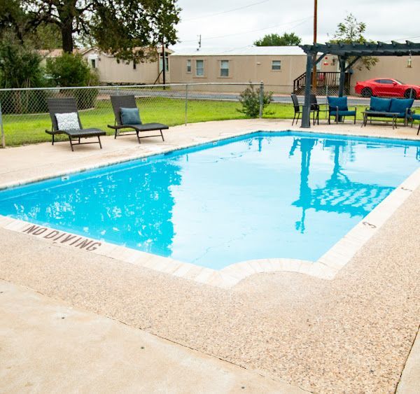 Swimming pool with lounge chairs, blue water, and a red car in the background. 