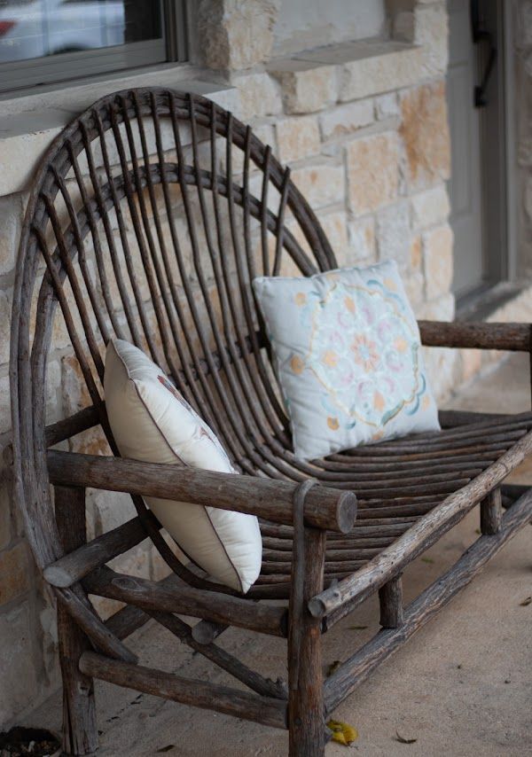 Wicker bench with two pillows against a stone wall.