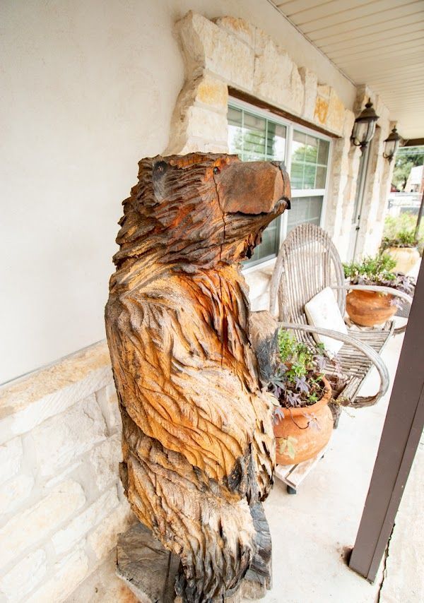 Wooden eagle sculpture on a porch next to potted plants, with stone detailing on the wall.