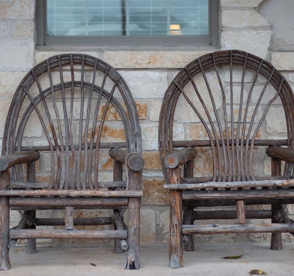 Two rustic wooden chairs with arched backs against a stone wall.