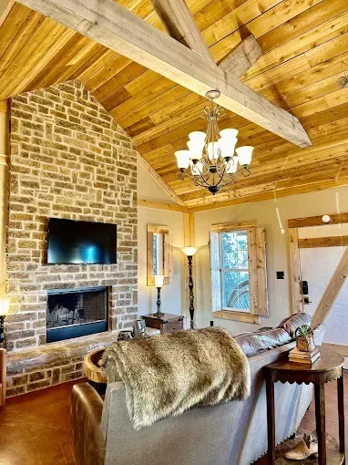 Living room with stone fireplace, vaulted wood ceiling, chandelier, and leather sofa.