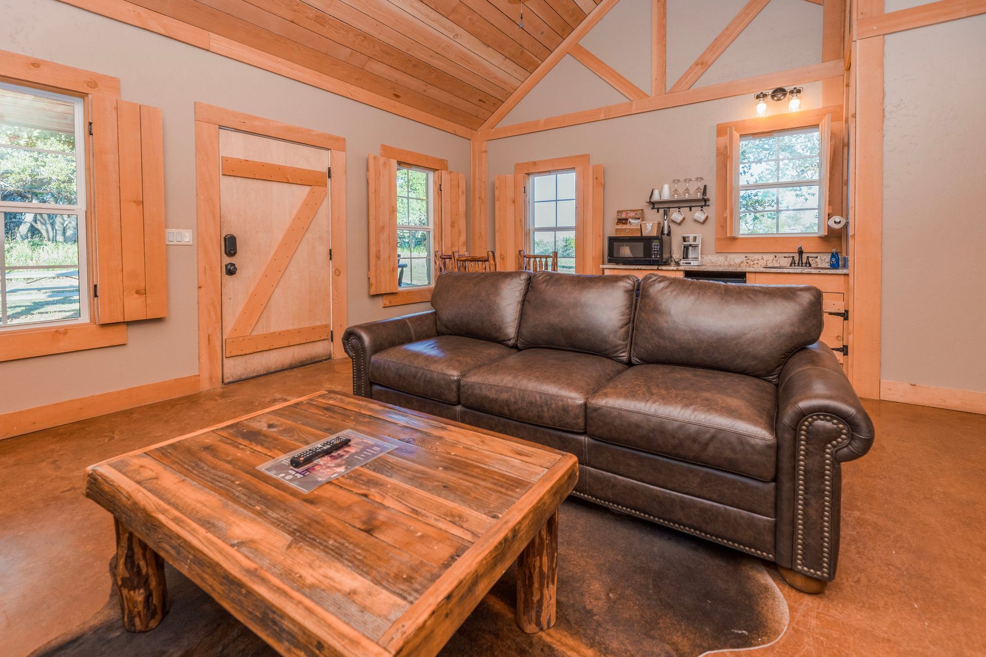 Living room with brown leather couch, wooden table, and kitchenette in a cabin.