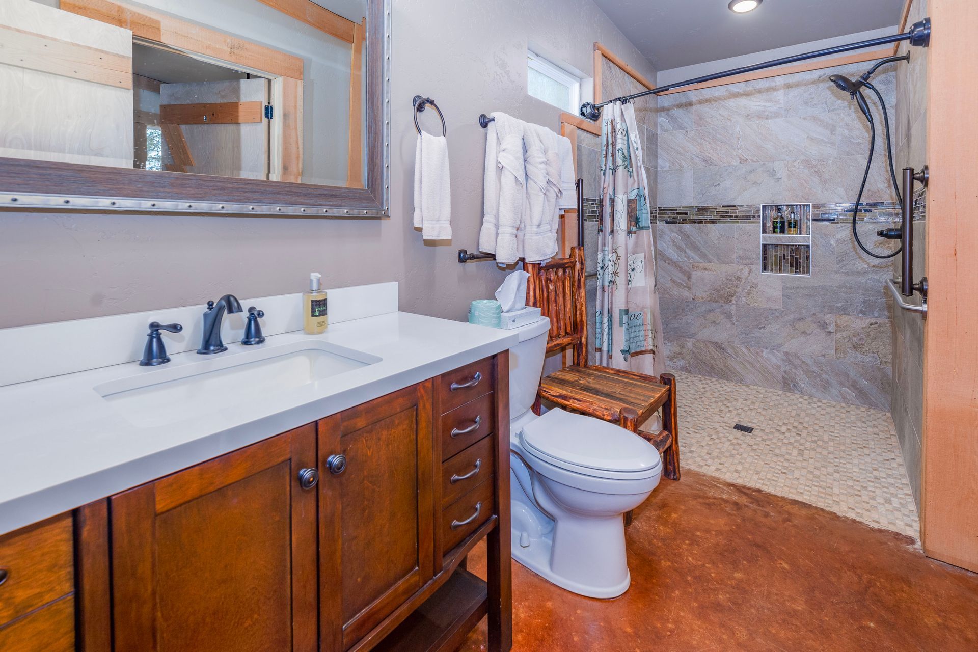 Bathroom with wooden vanity, white countertop, and a stone-tiled shower. Brown floor, beige walls.