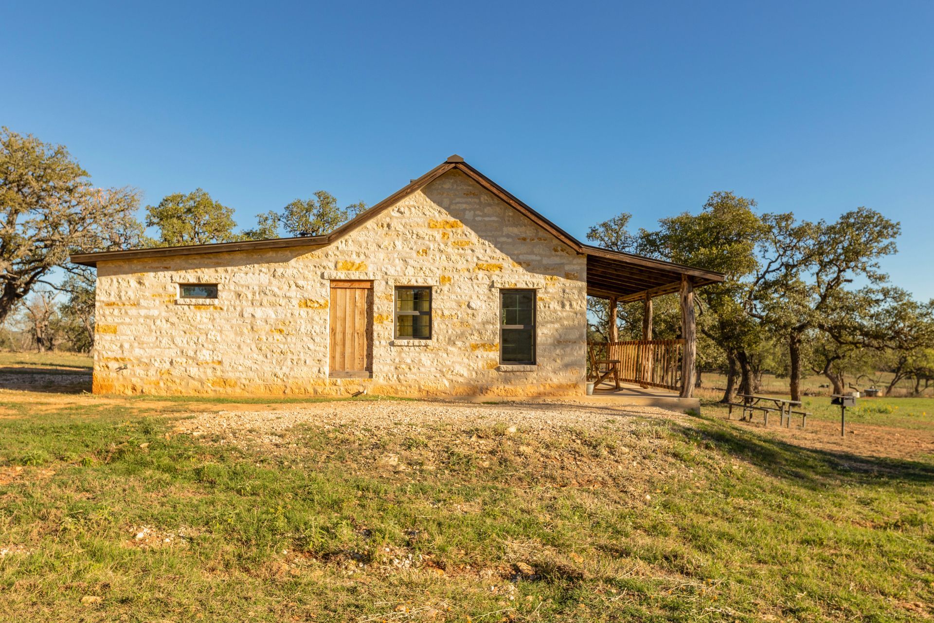 Stone cabin with porch and wooden door in a grassy field under a blue sky.
