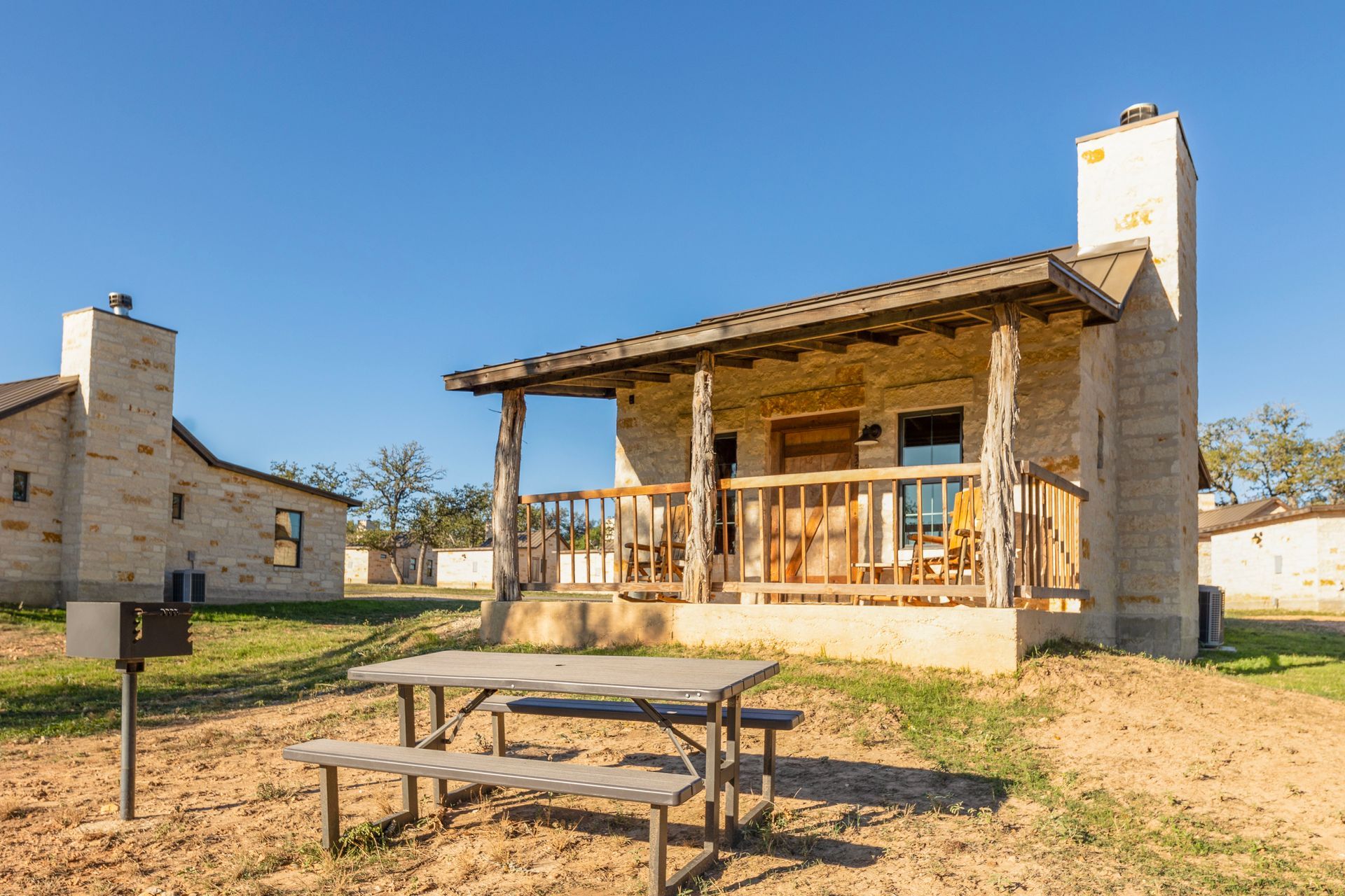 Stone cabin with porch and picnic table on a sunny day.