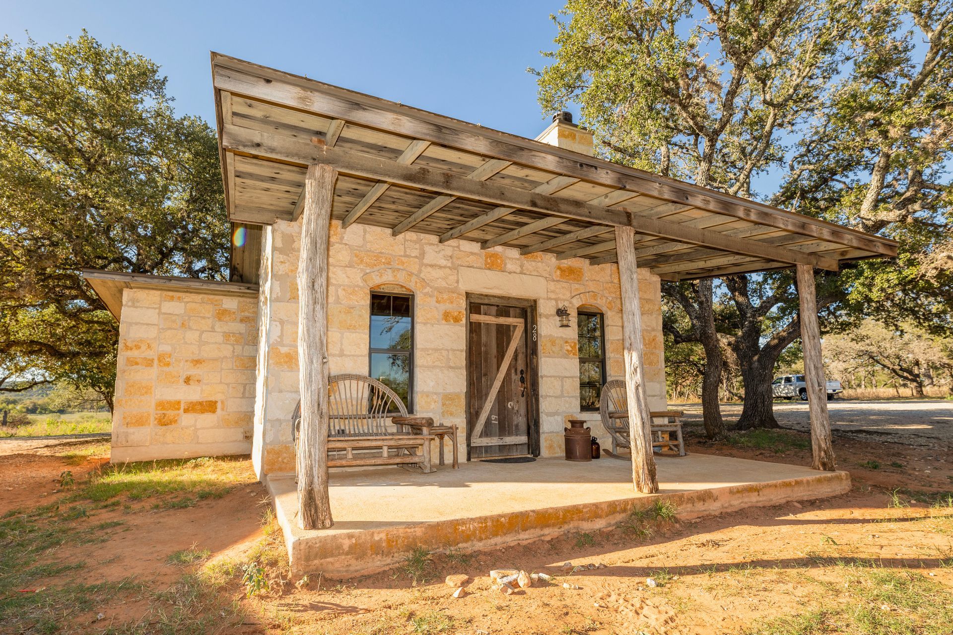 Stone cottage with porch, wooden posts, and a rustic door, set in a sunny outdoor area.