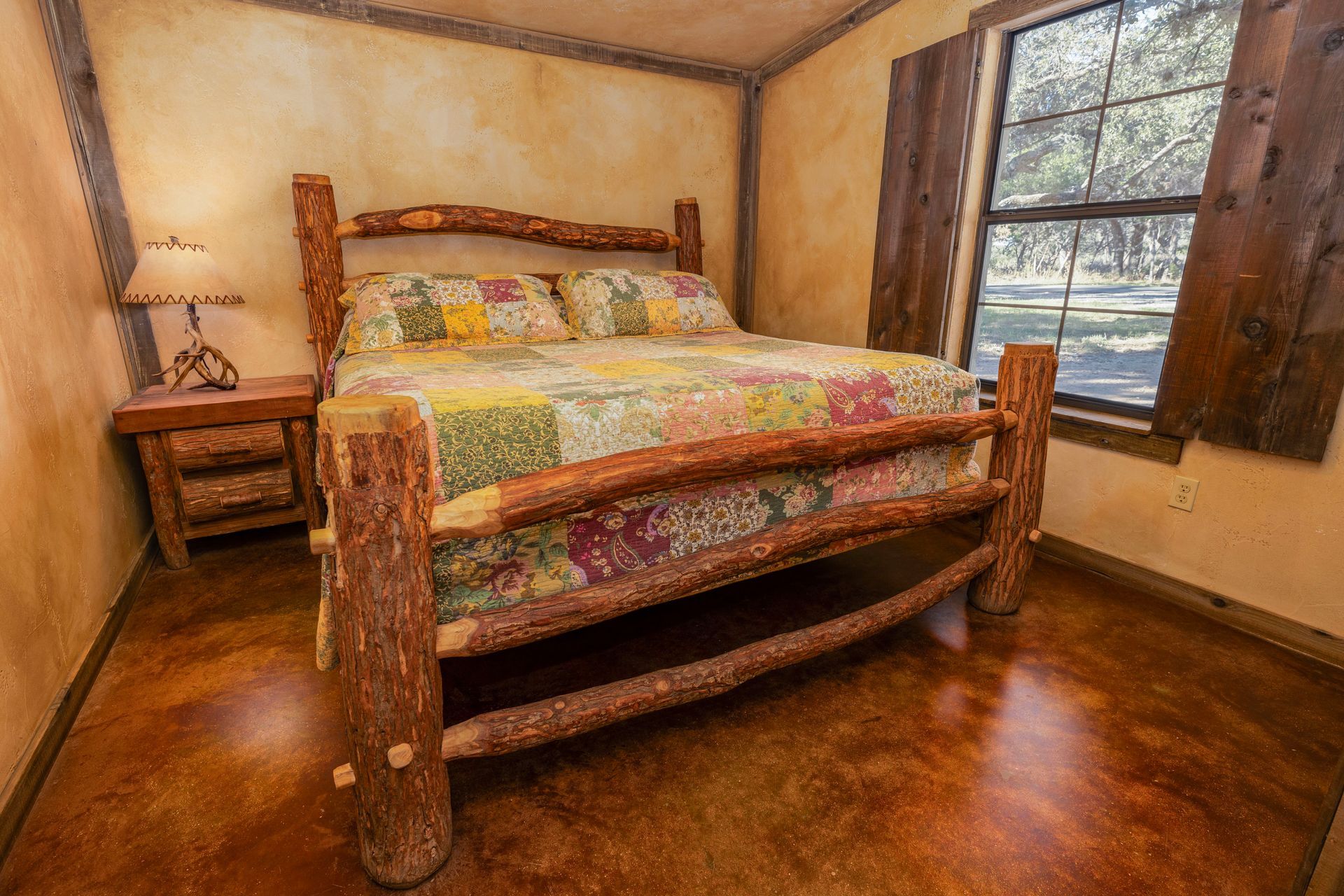 Bedroom with rustic log bed, patchwork quilt, small nightstand, and window with shutters.
