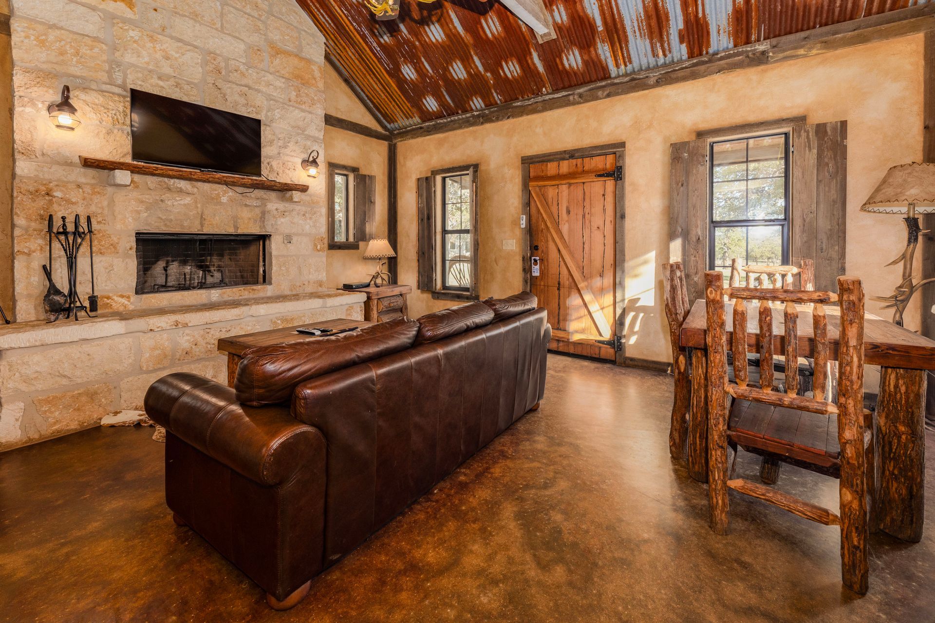 Rustic cabin interior with leather sofa, fireplace, and wood table.