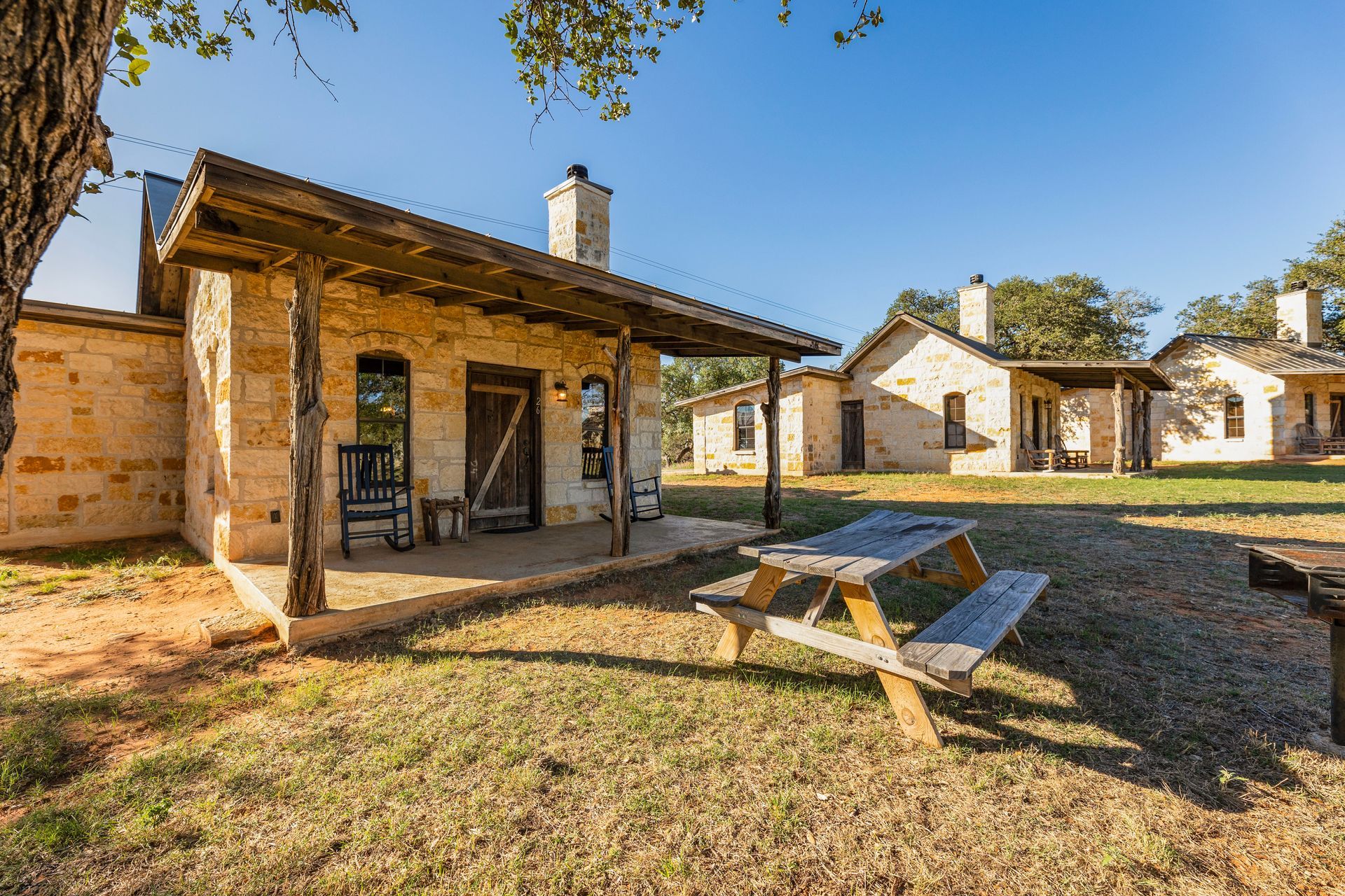 Stone cabins with wooden porches and a picnic table on a grassy lawn.