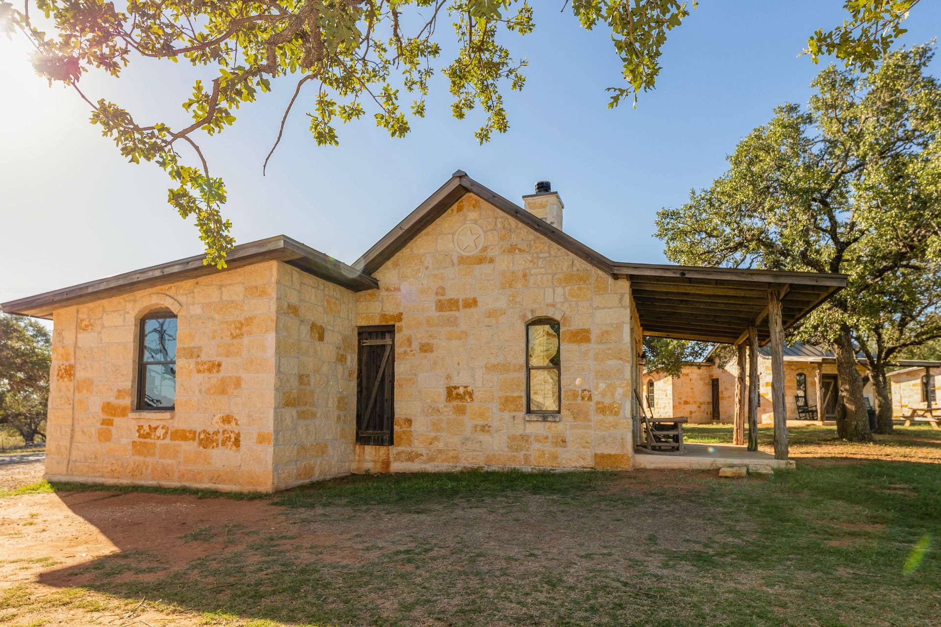 Stone house with a covered porch, under a blue sky and tree branches.
