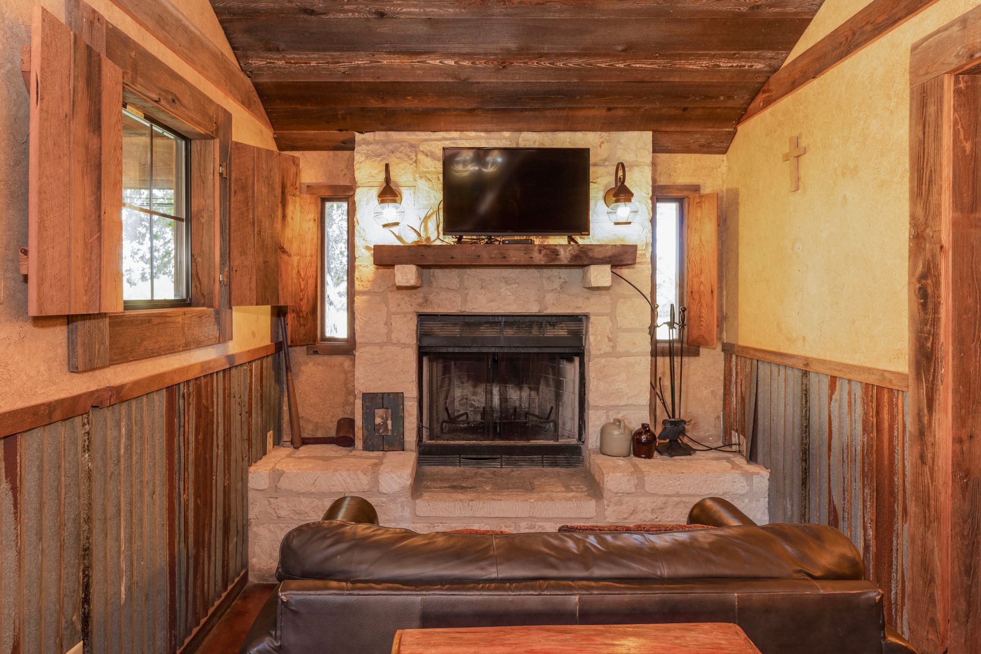 Cozy cabin living room with stone fireplace, TV, wood paneling, and a leather couch.
