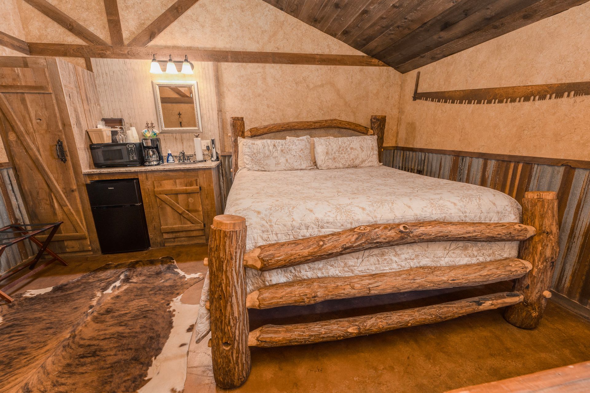 Rustic bedroom with wooden bed frame, kitchenette, and animal hide rug.