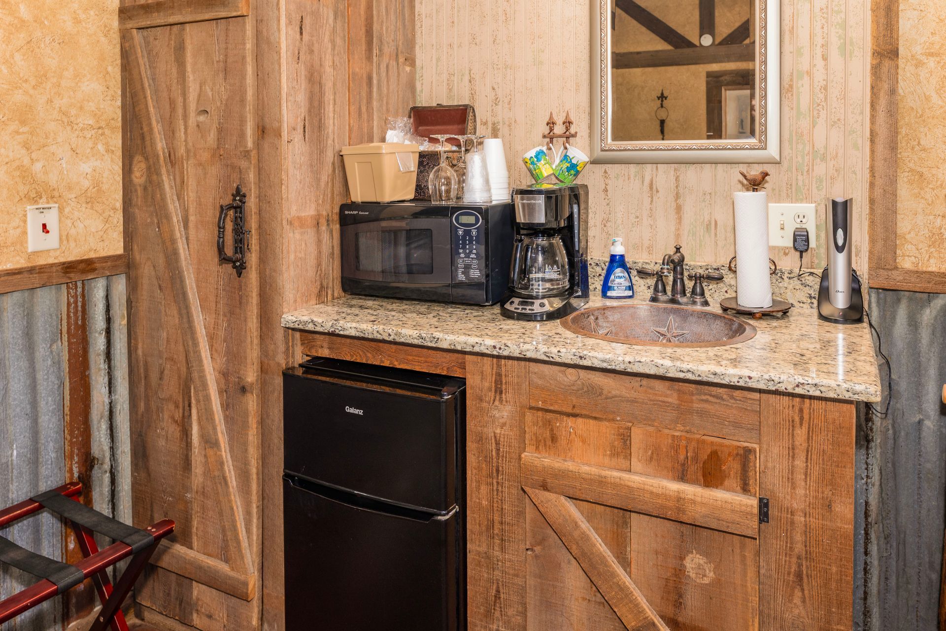 Small kitchenette with microwave, coffee maker, sink, and mini-fridge in a rustic room.