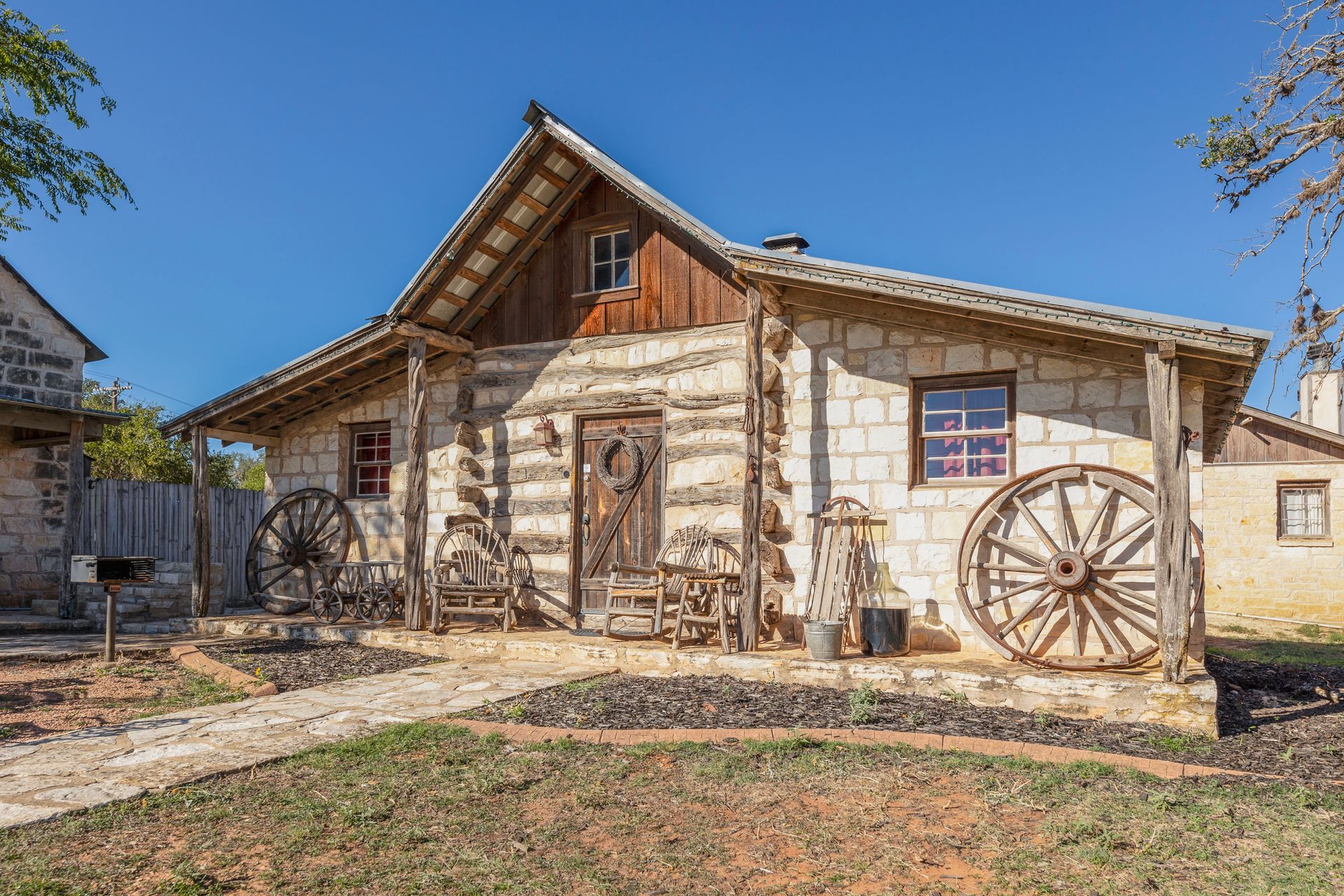 Rustic cabin with stone walls, wooden porch, wagon wheels, and blue sky.