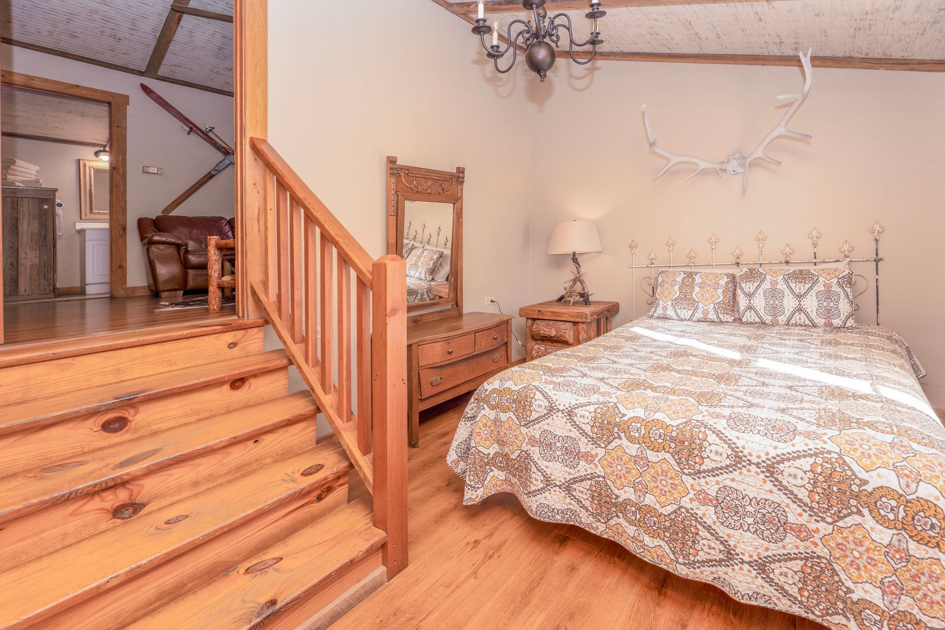 Bedroom with staircase, wooden furniture, white walls, and a patterned bedspread.