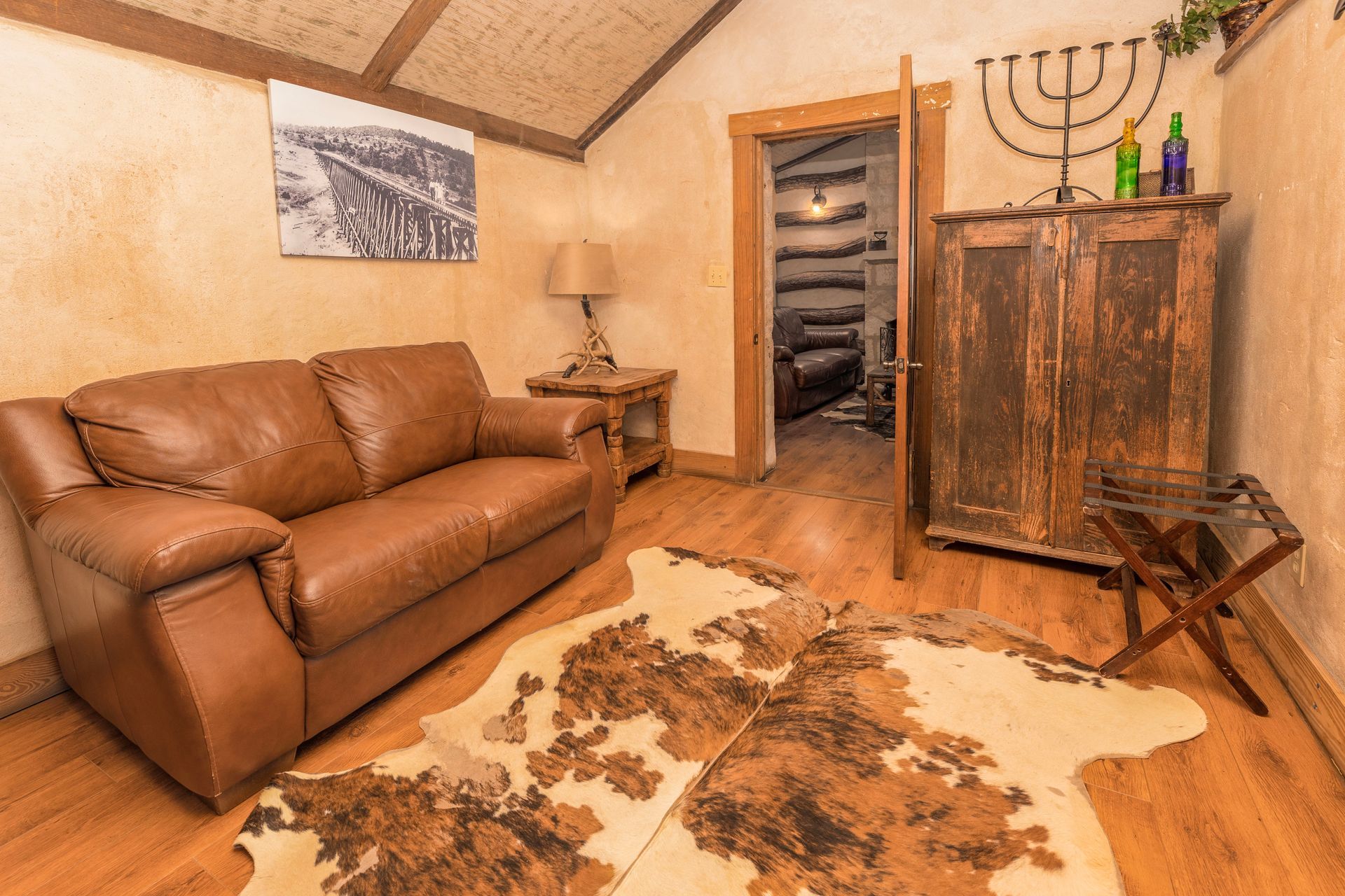 Cozy room with leather sofa, cowhide rug, wooden cabinet, and doorway leading to another room.