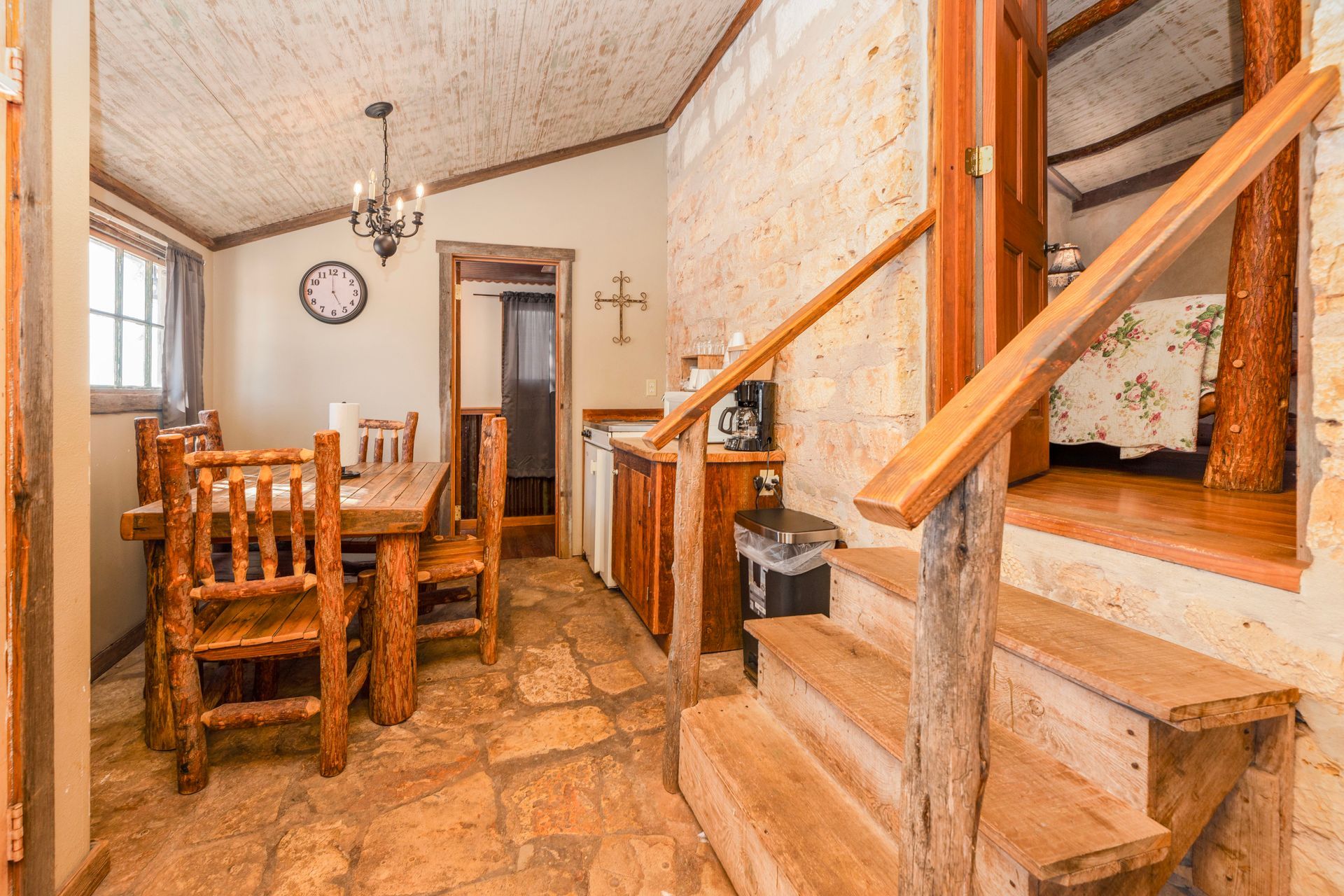 Rustic dining area with wooden table, chairs, and staircase leading to a higher level.