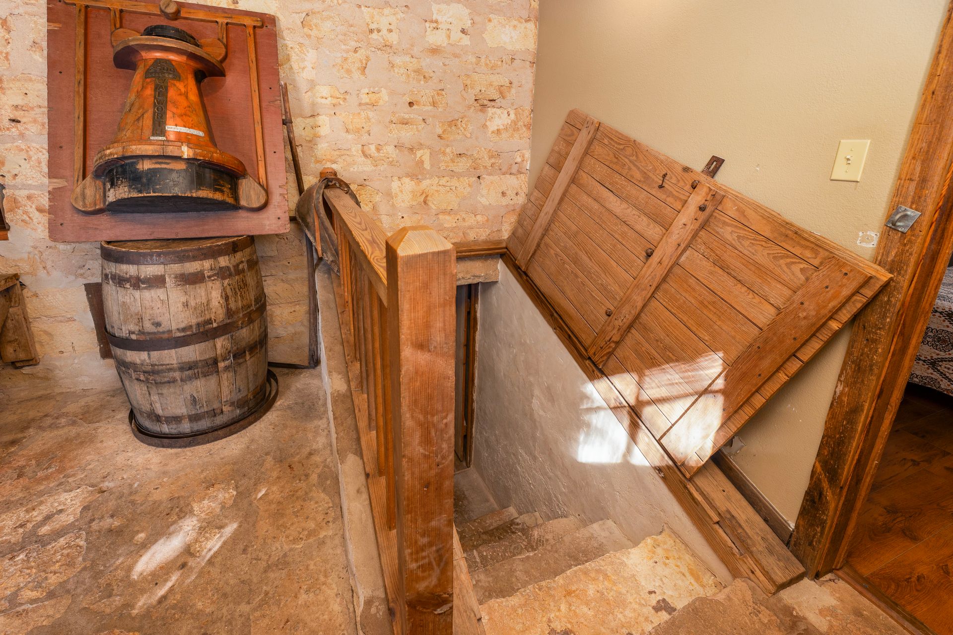 Stairwell with open wooden door leading down to basement. Beside it are a barrel and a decorative object.
