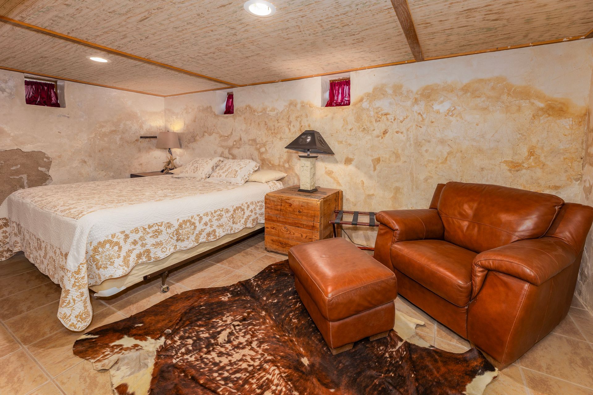 Bedroom with bed, leather chair, ottoman, rug, and rustic walls.