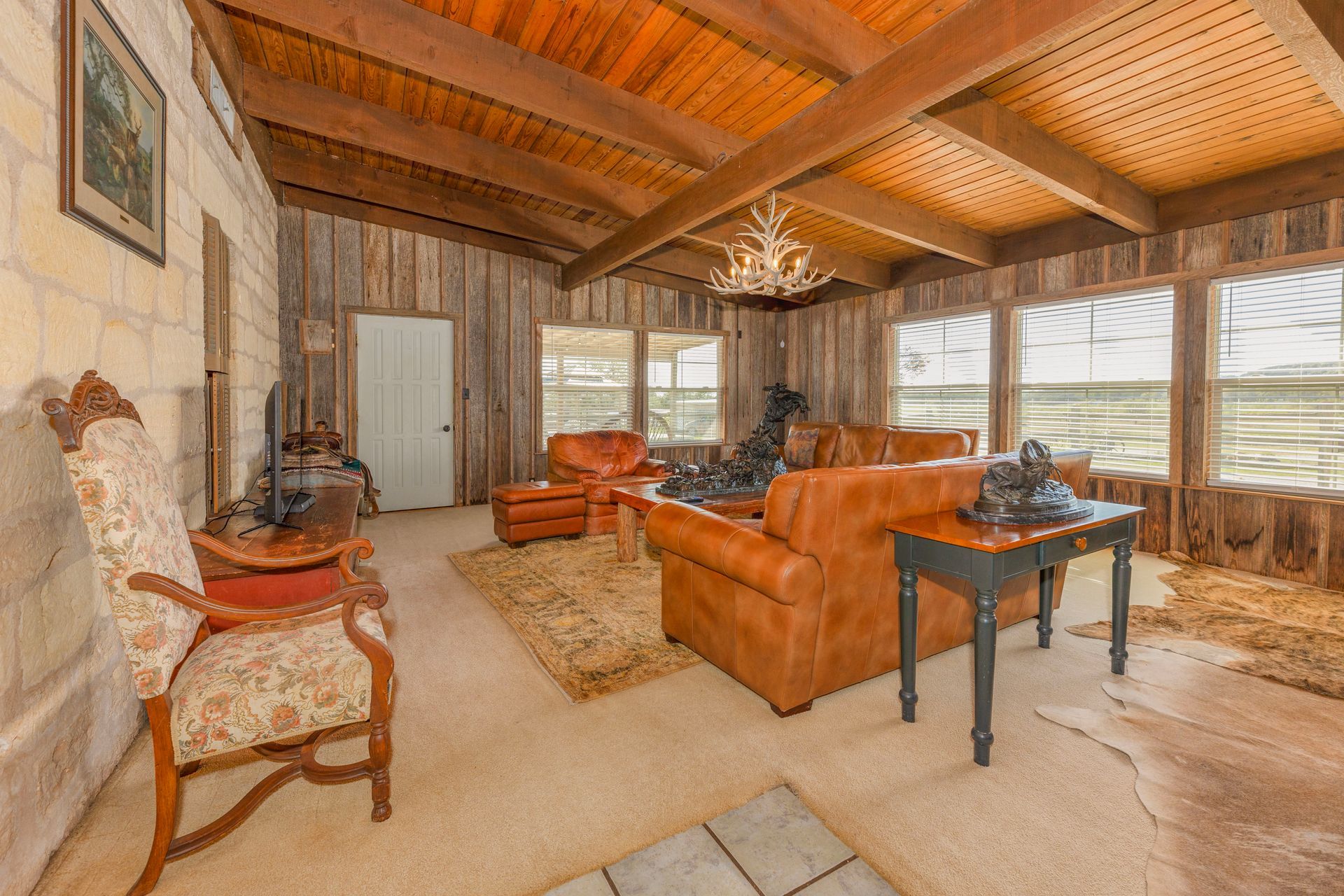 Living room with wood ceiling, leather furniture, and stone walls.