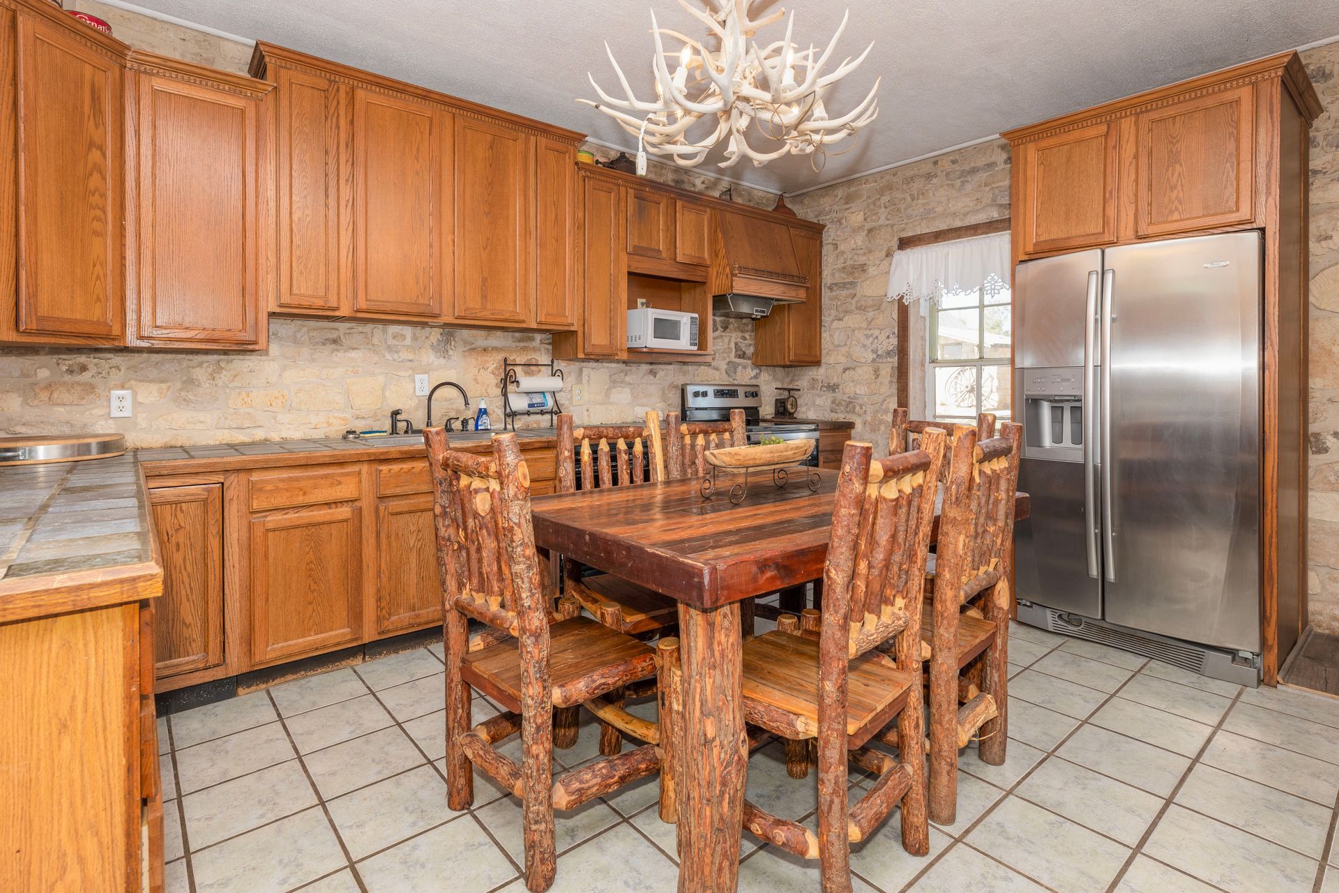 Rustic kitchen with wooden cabinets, dining table, and stainless steel refrigerator.