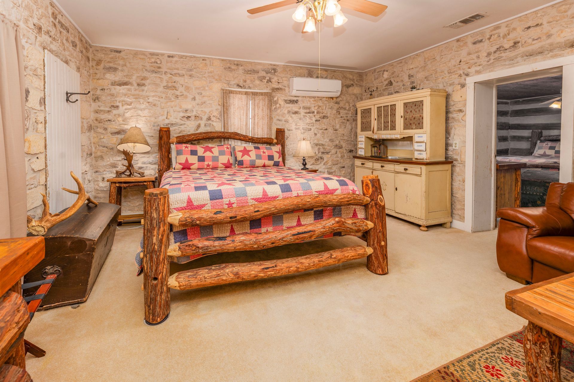 Rustic bedroom with stone walls, a log bed, and a small cream-colored hutch.