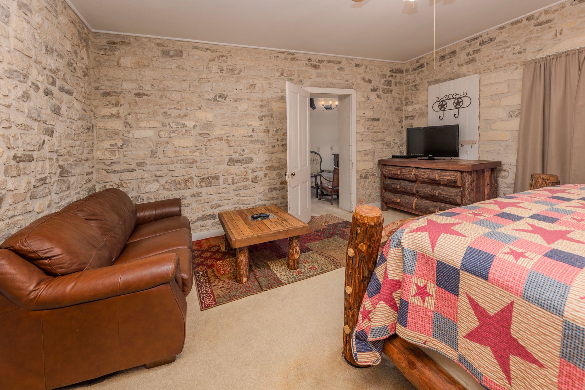 Bedroom with stone walls, leather sofa, wooden bed, TV, and small rug.