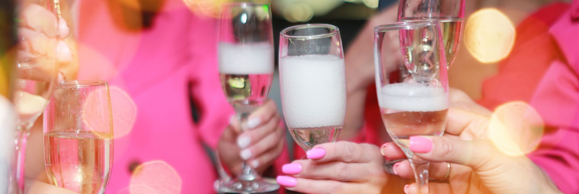 People toasting with champagne flutes; pink outfits, bokeh background.