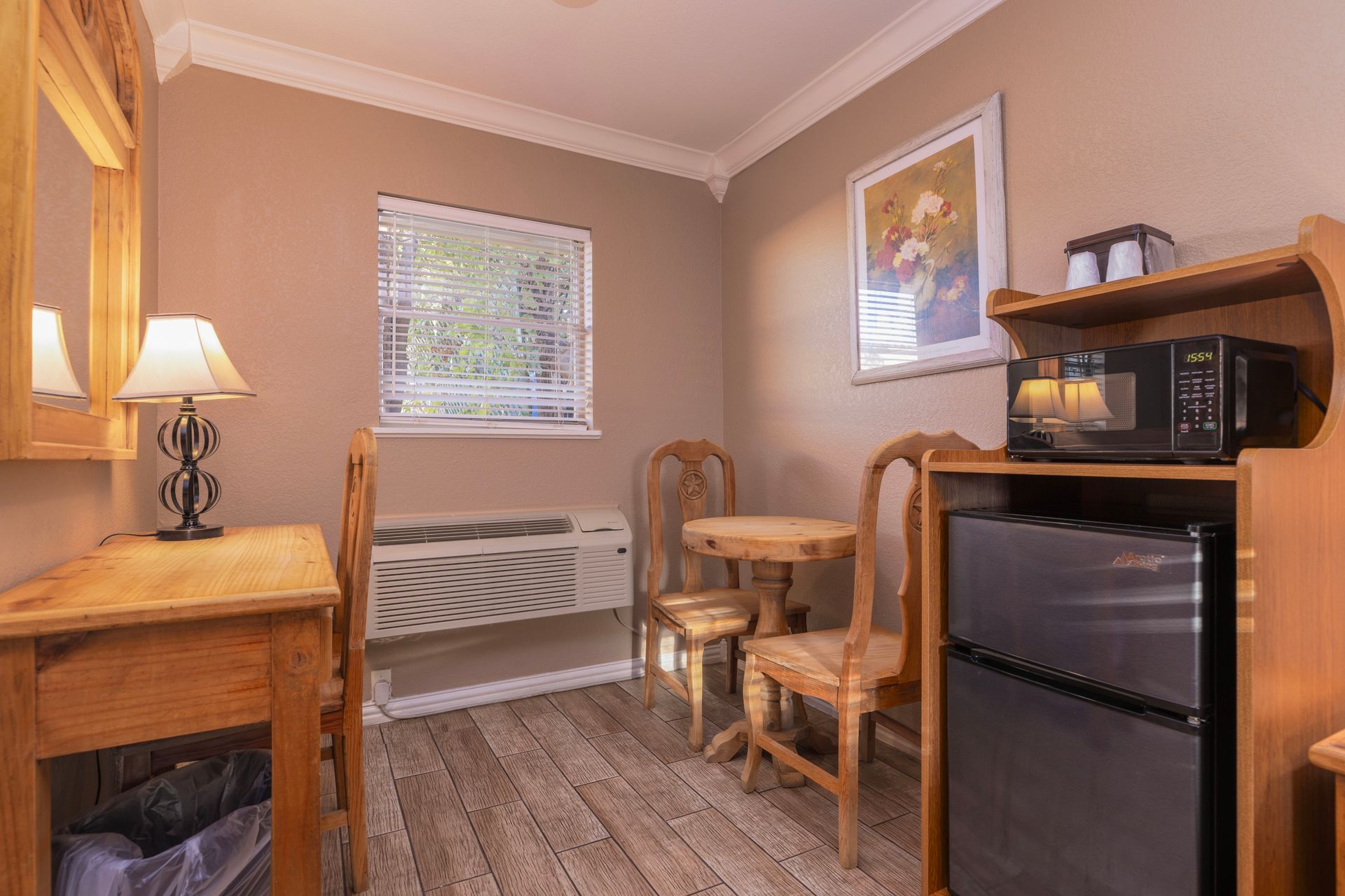 Small hotel room with desk, table, chairs, microwave, mini fridge, and window.