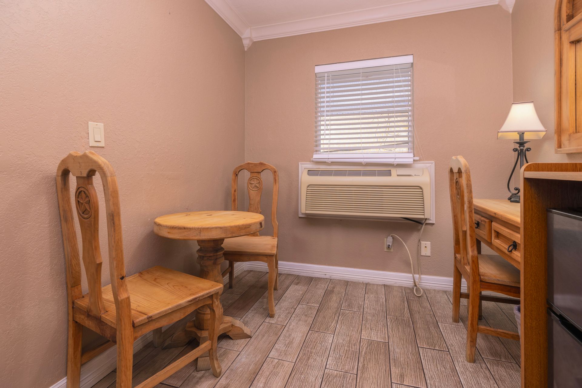Small room with table, chairs, desk, window air conditioner, and hardwood floors.