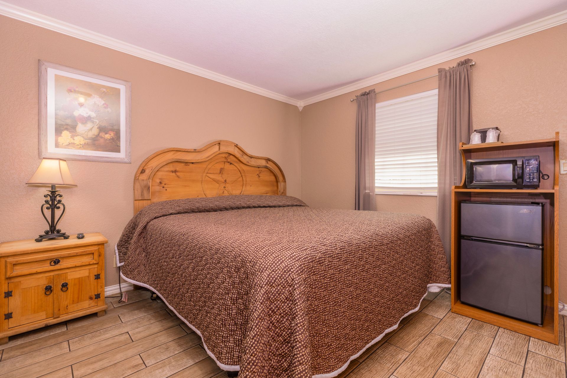 Bedroom with a bed, nightstand, picture, window, microwave, and refrigerator.