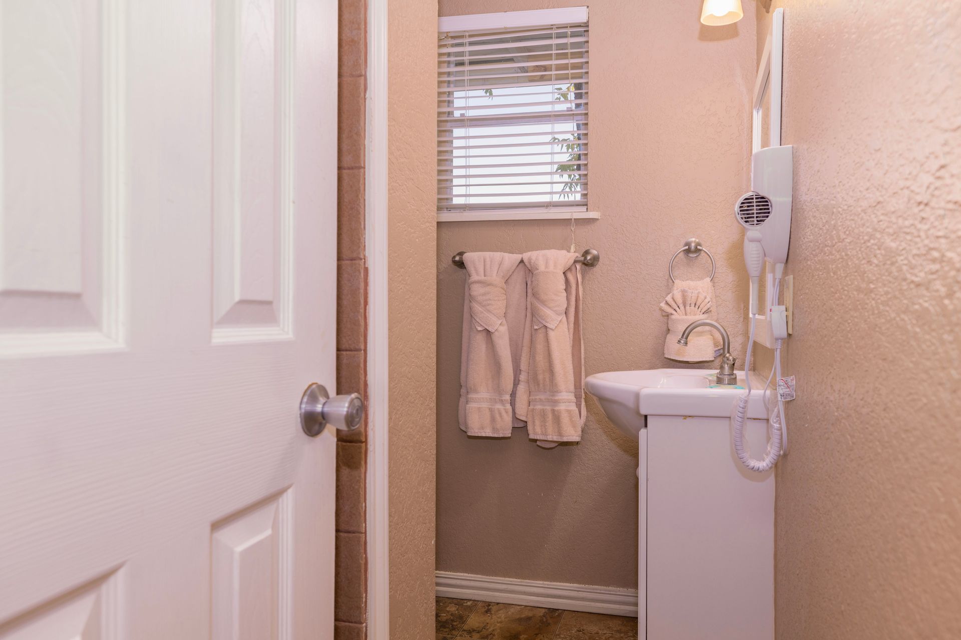 Small bathroom with a sink, towel rack, window with blinds, and mounted hair dryer.