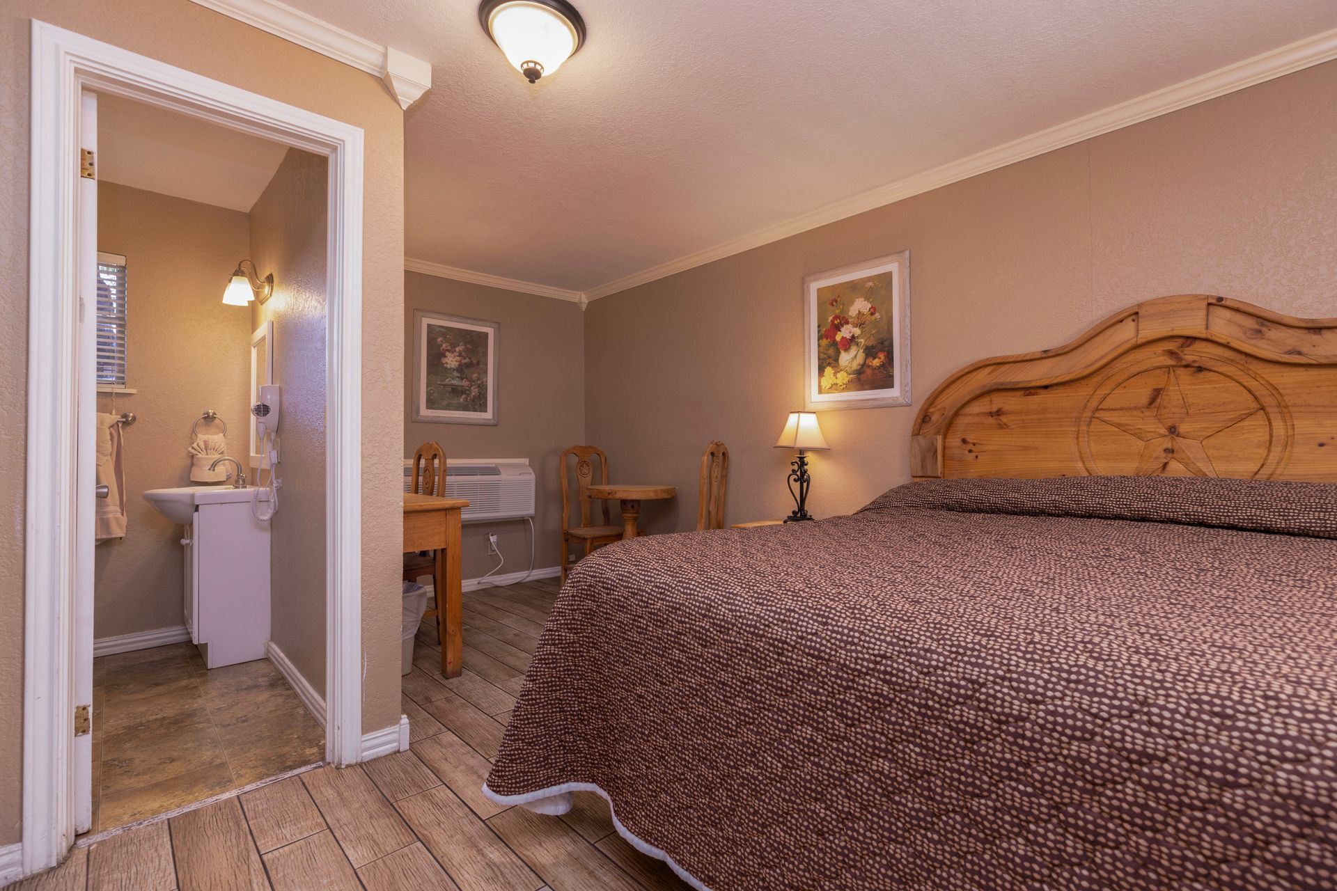 Bedroom with a brown bedspread and headboard, wood floors, and a bathroom visible in doorway.