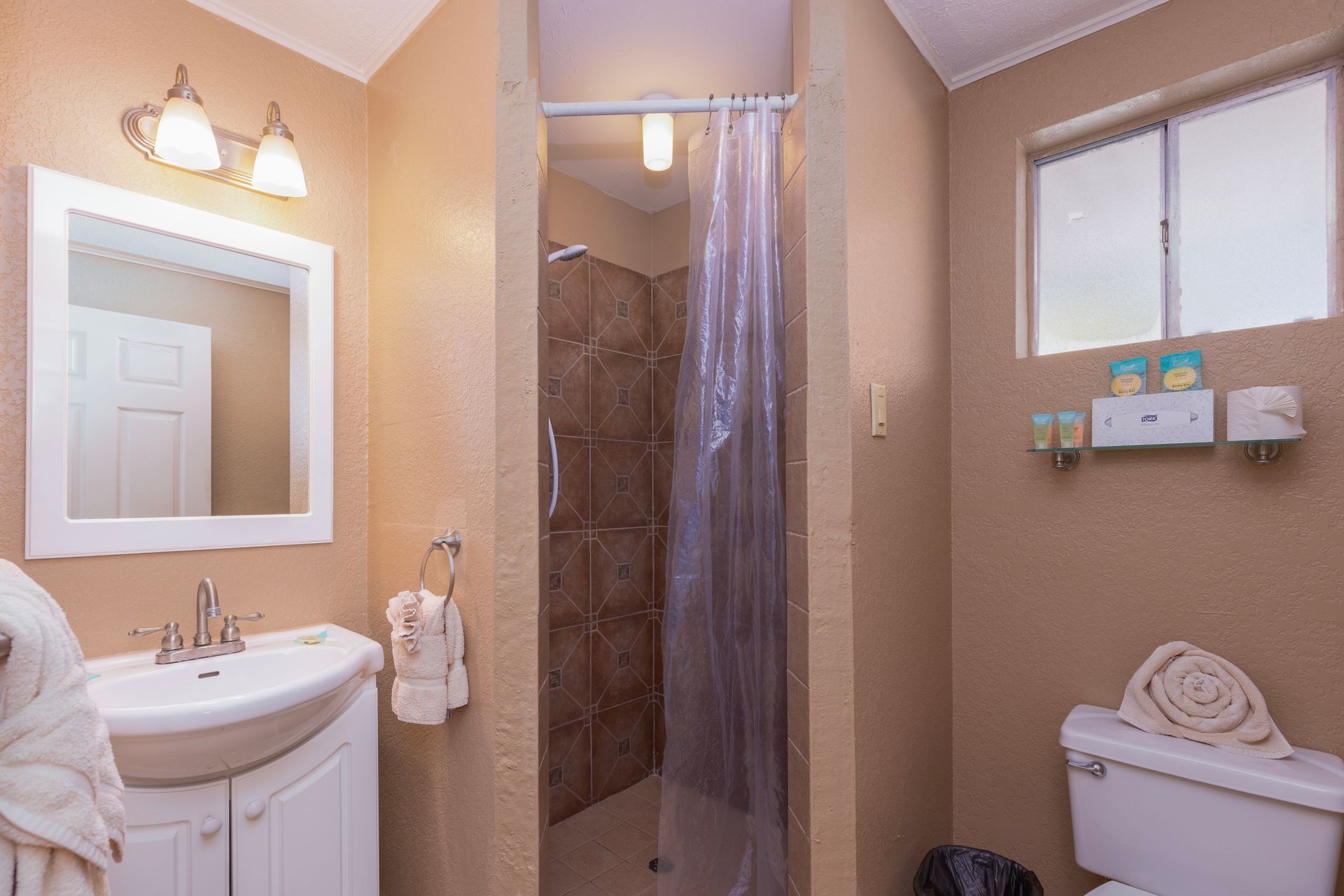 Bathroom with sink, toilet, shower, and window. Beige walls.