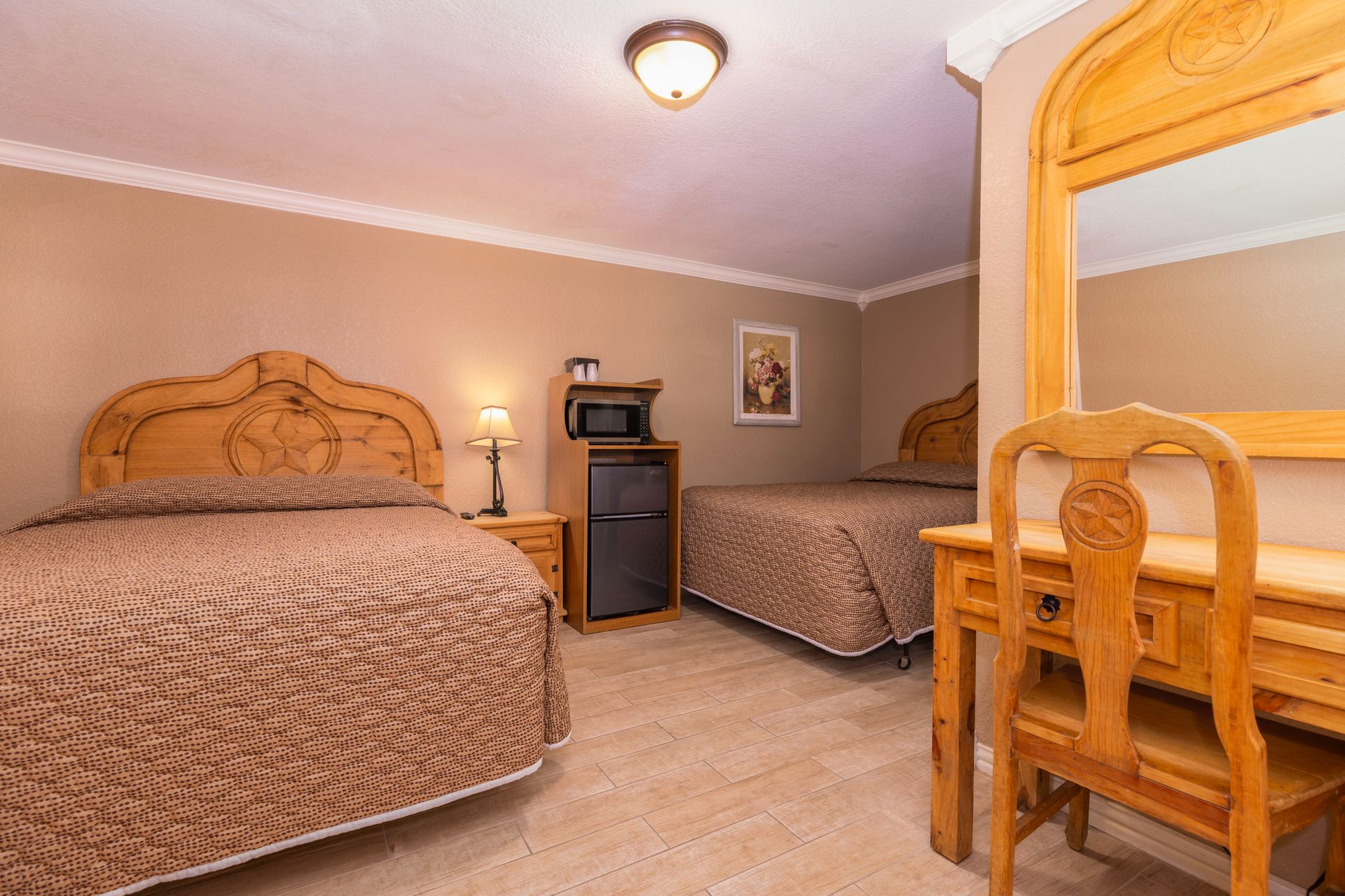 Hotel room with two beds, a desk, and a mini-fridge. Beige walls, brown bedspreads, and wood furniture.