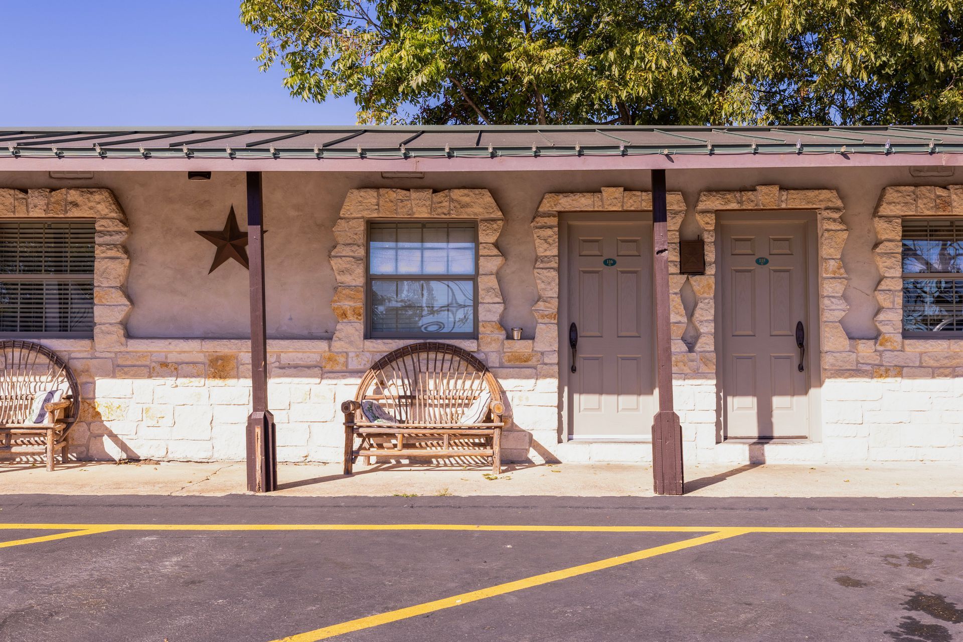 Exterior of a motel building with stone facade, doors, windows, and a star decoration; benches in front.