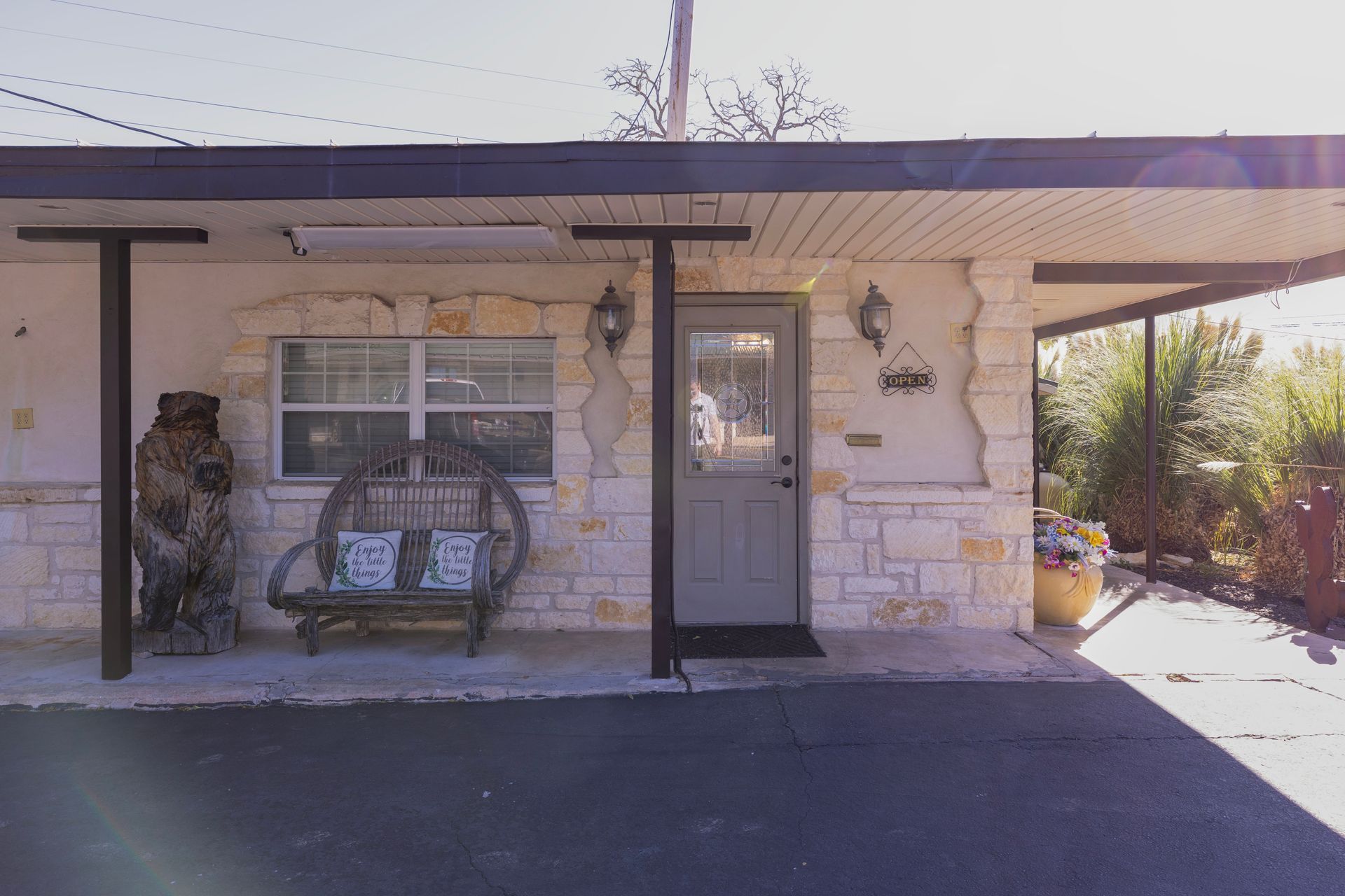 Exterior of a one-story building with a tan and stone facade, door, and awning. Bench outside the window.