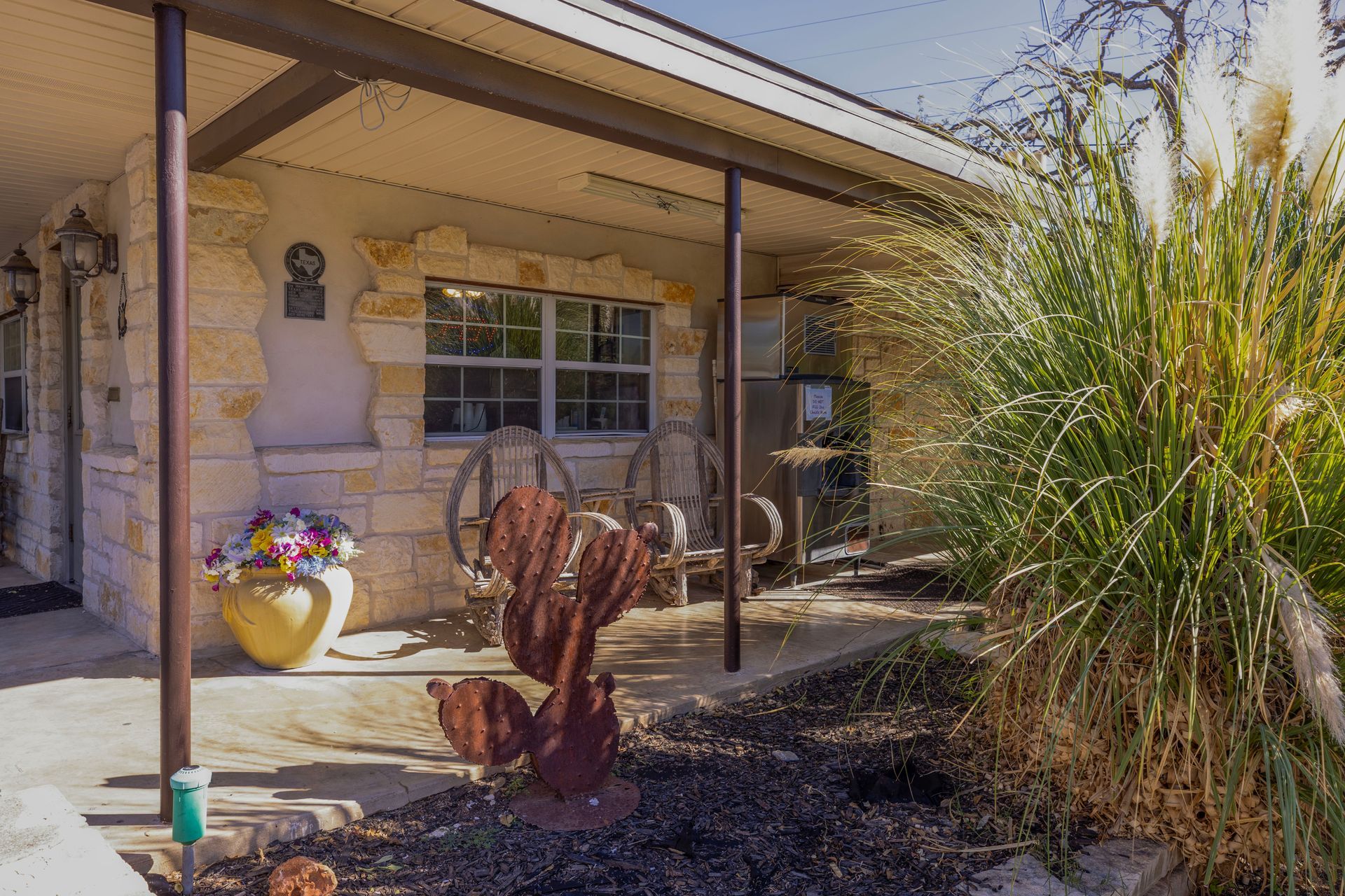 Stone house with porch, cactus sculpture, decorative wagon wheels, and tall grass.