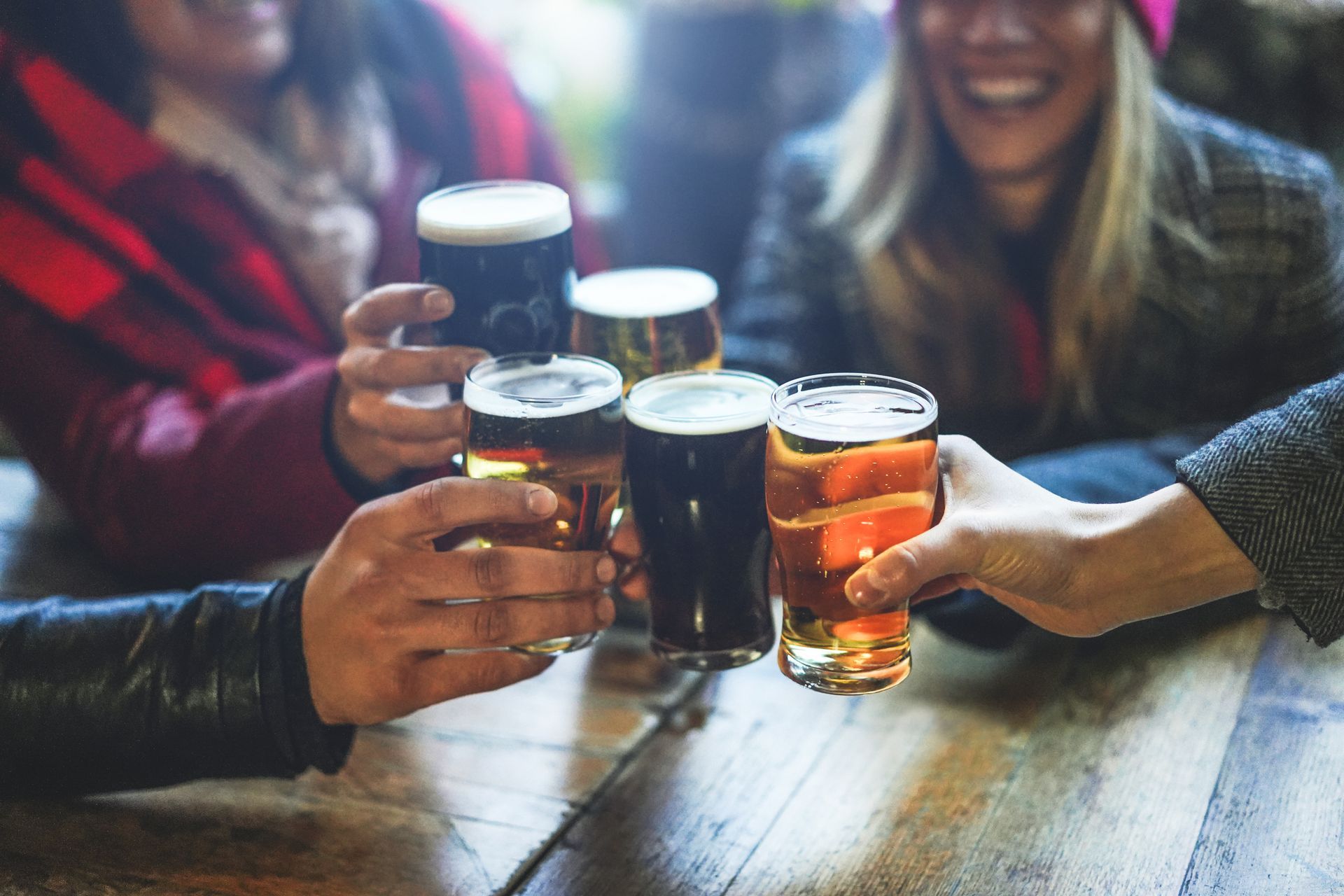 Friends toasting with beer glasses at a table, smiling.