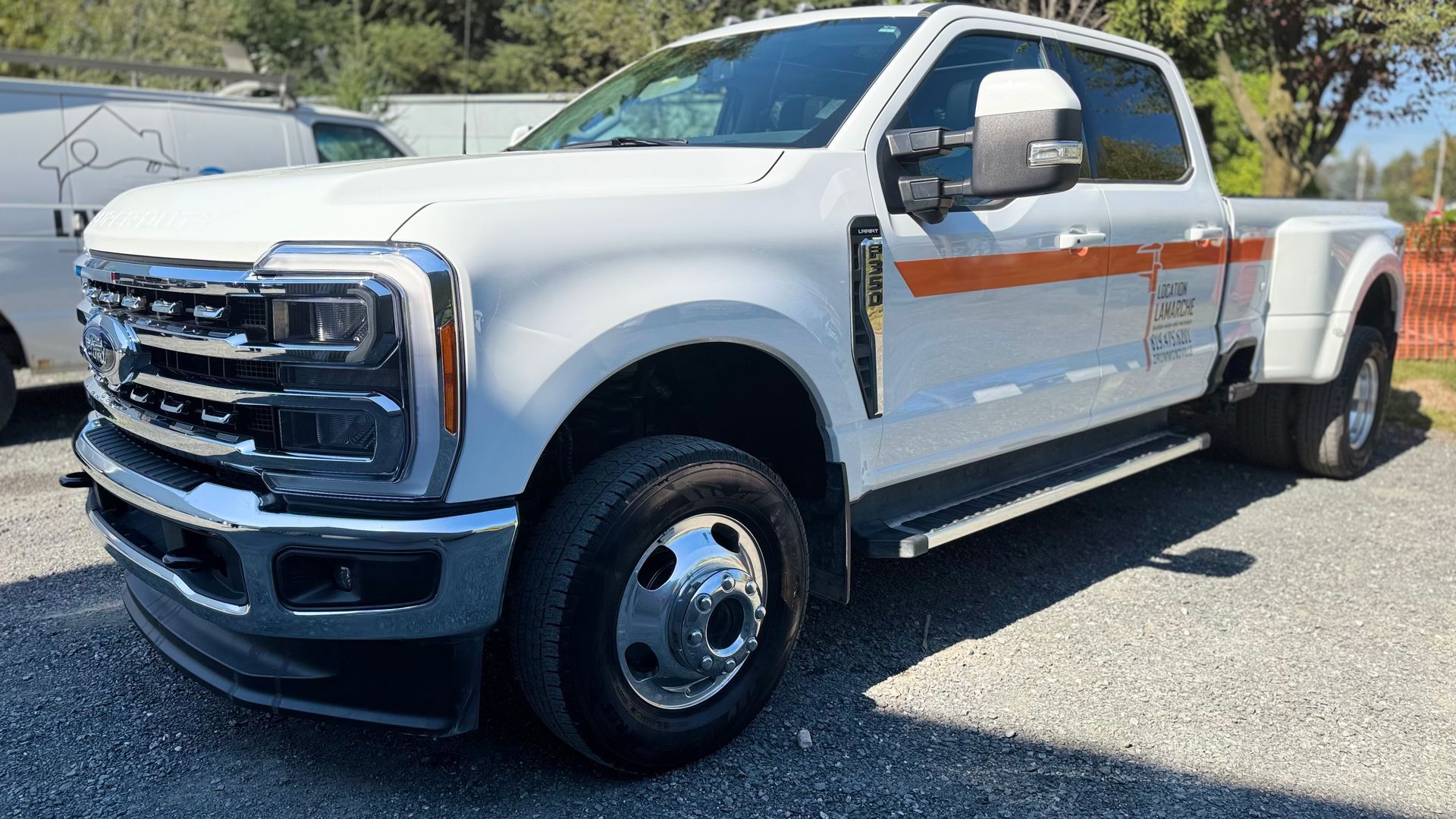 Camion Ford F-350 double cabine blanc, bande orange, garé à l'extérieur par une journée ensoleillée.