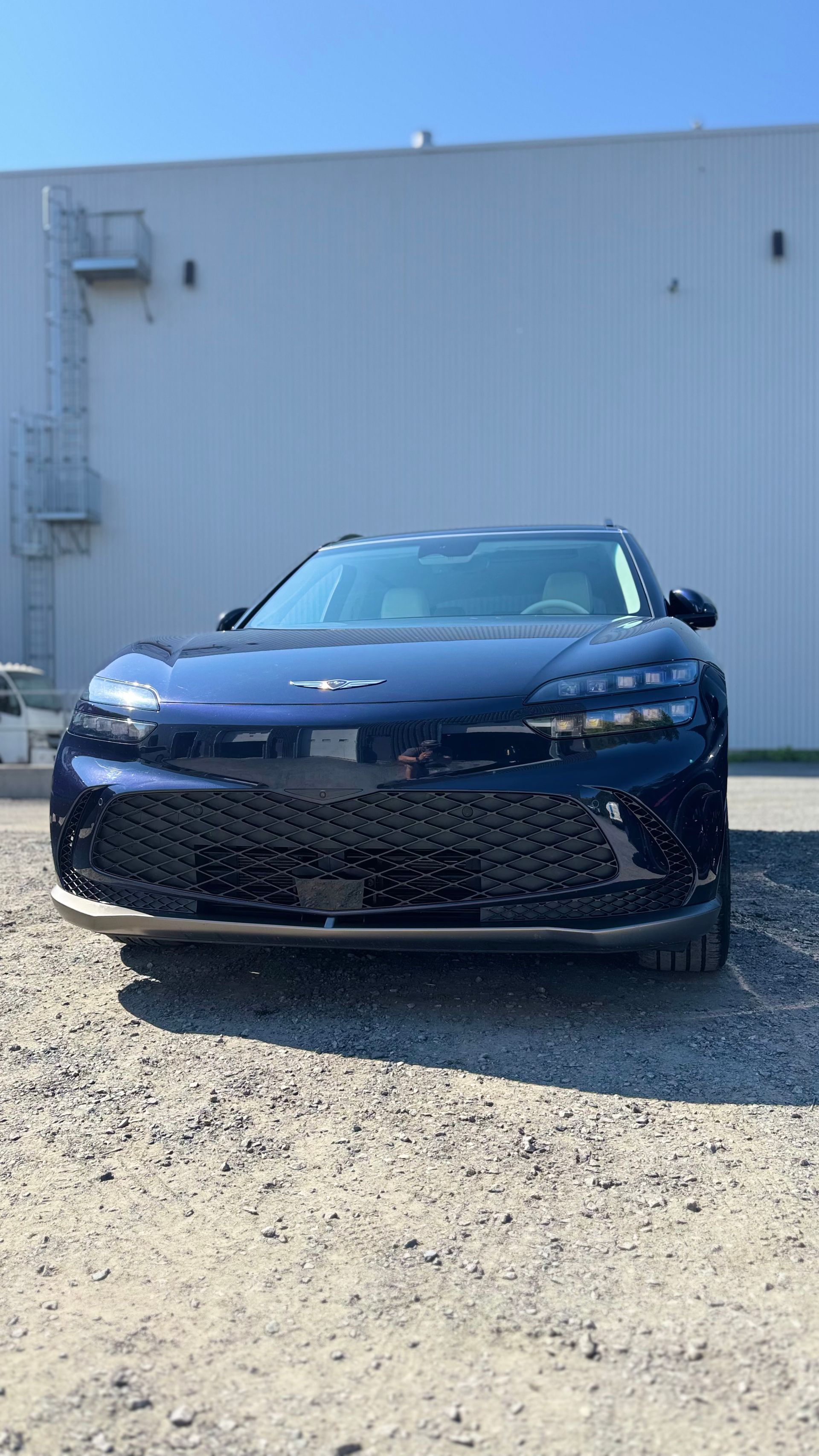 Voiture électrique Lucid Air bleu foncé garée devant un bâtiment gris clair sur un terrain en gravier.