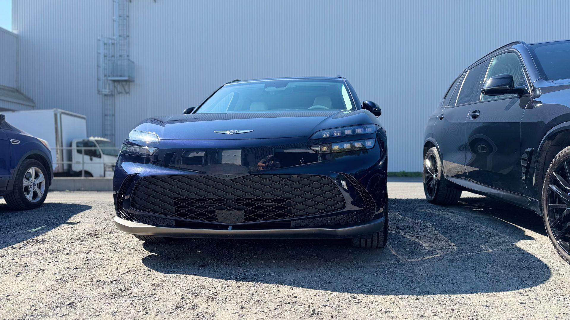 SUV bleu garé entre deux autres voitures sur un terrain sous un ciel ensoleillé.