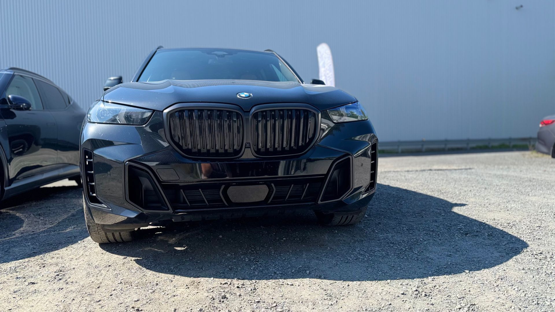 SUV BMW noir garé à l'extérieur par une journée ensoleillée, avec une calandre noircie.