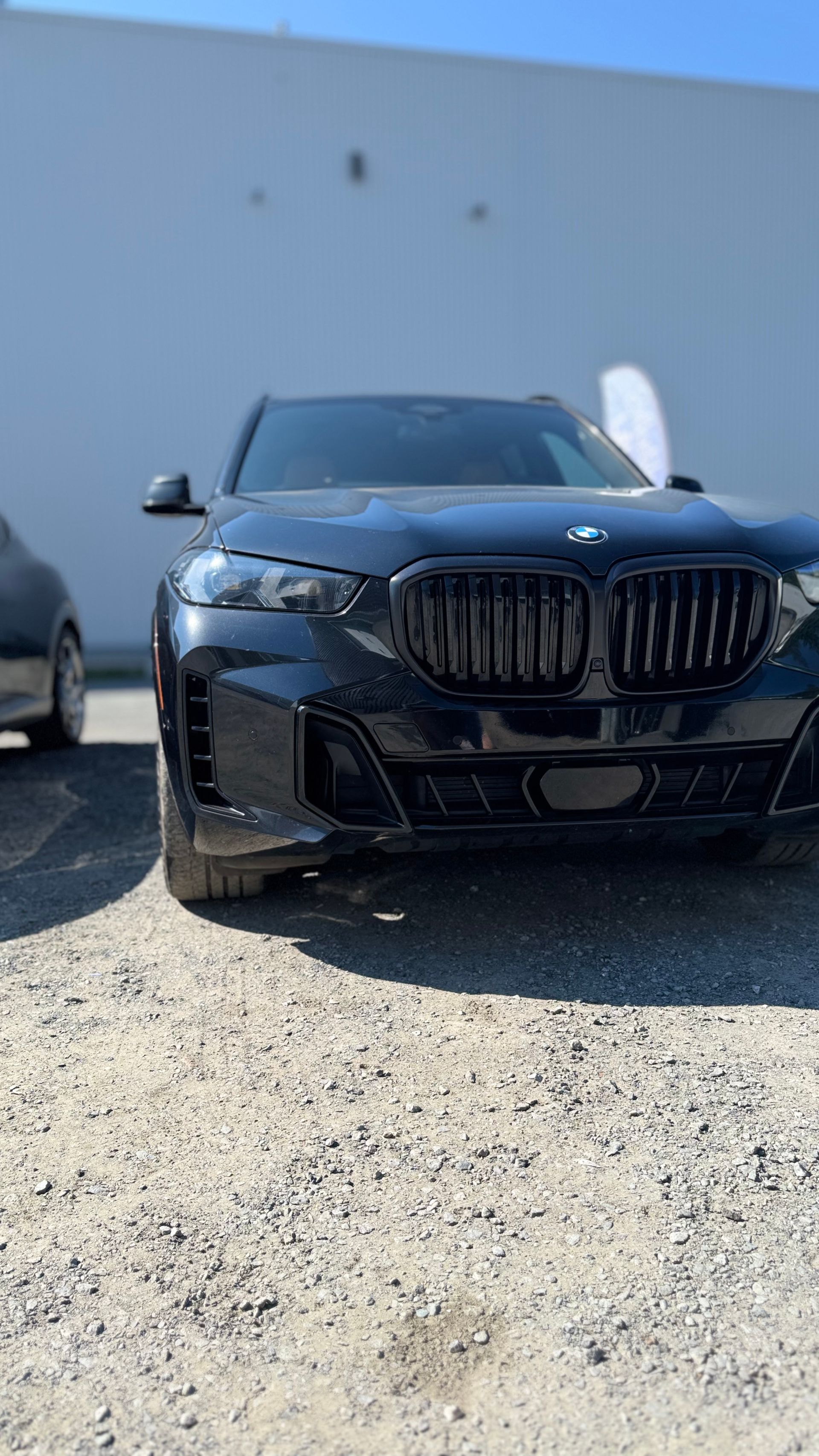 SUV BMW noir garé devant un bâtiment de couleur claire par une journée ensoleillée.