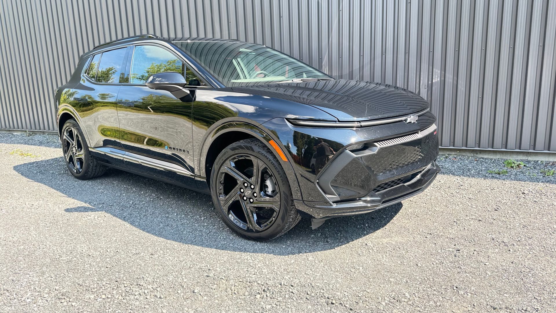 SUV électrique Chevrolet Equinox noir garé sur du gravier devant un mur en bois gris.