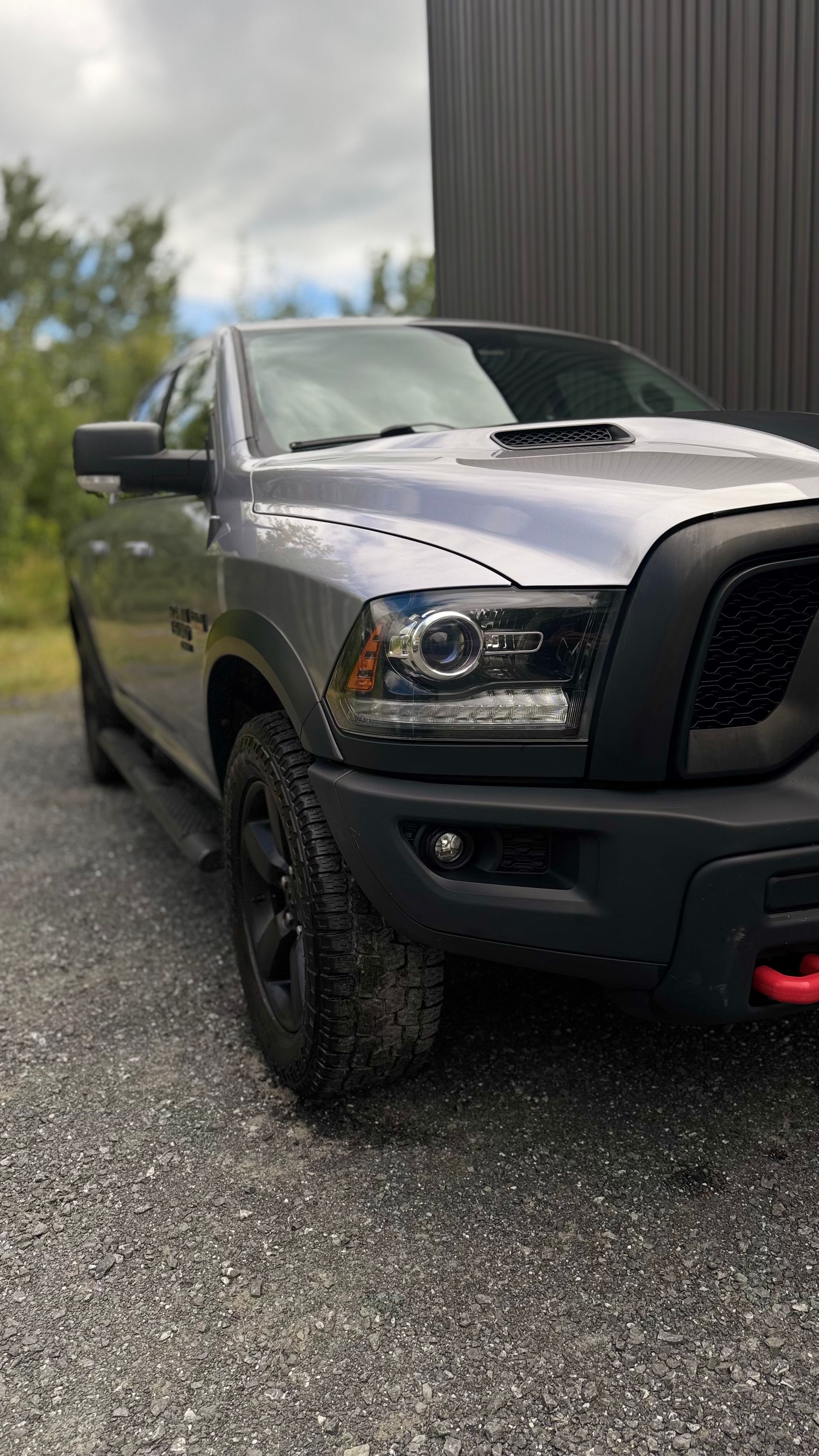 Camionnette Ram grise stationnée sur du gravier, avec garniture noire et crochet de remorquage rouge.