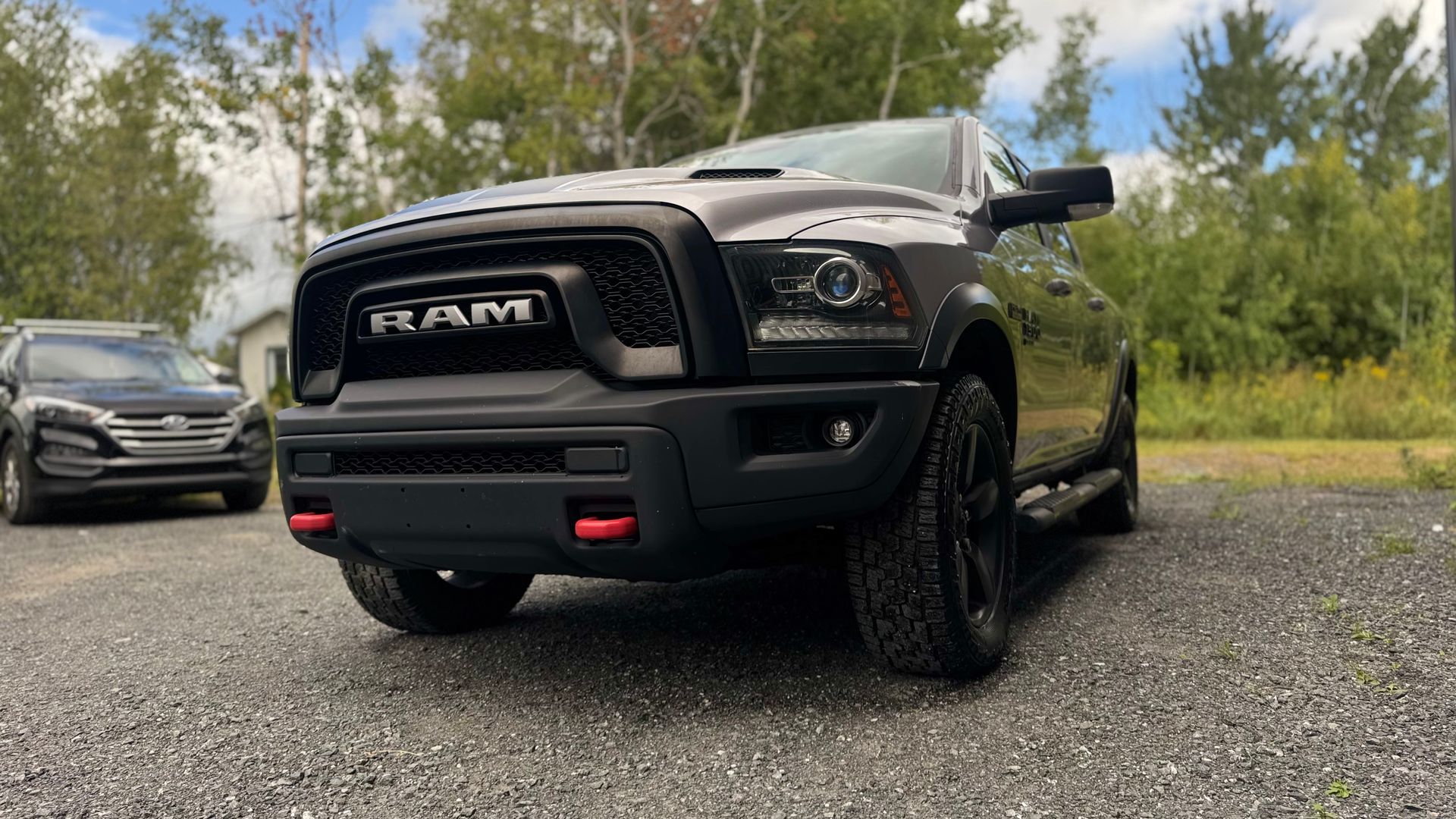 Camion RAM noir garé sur du gravier avec un SUV sombre en arrière-plan ; des arbres au loin.