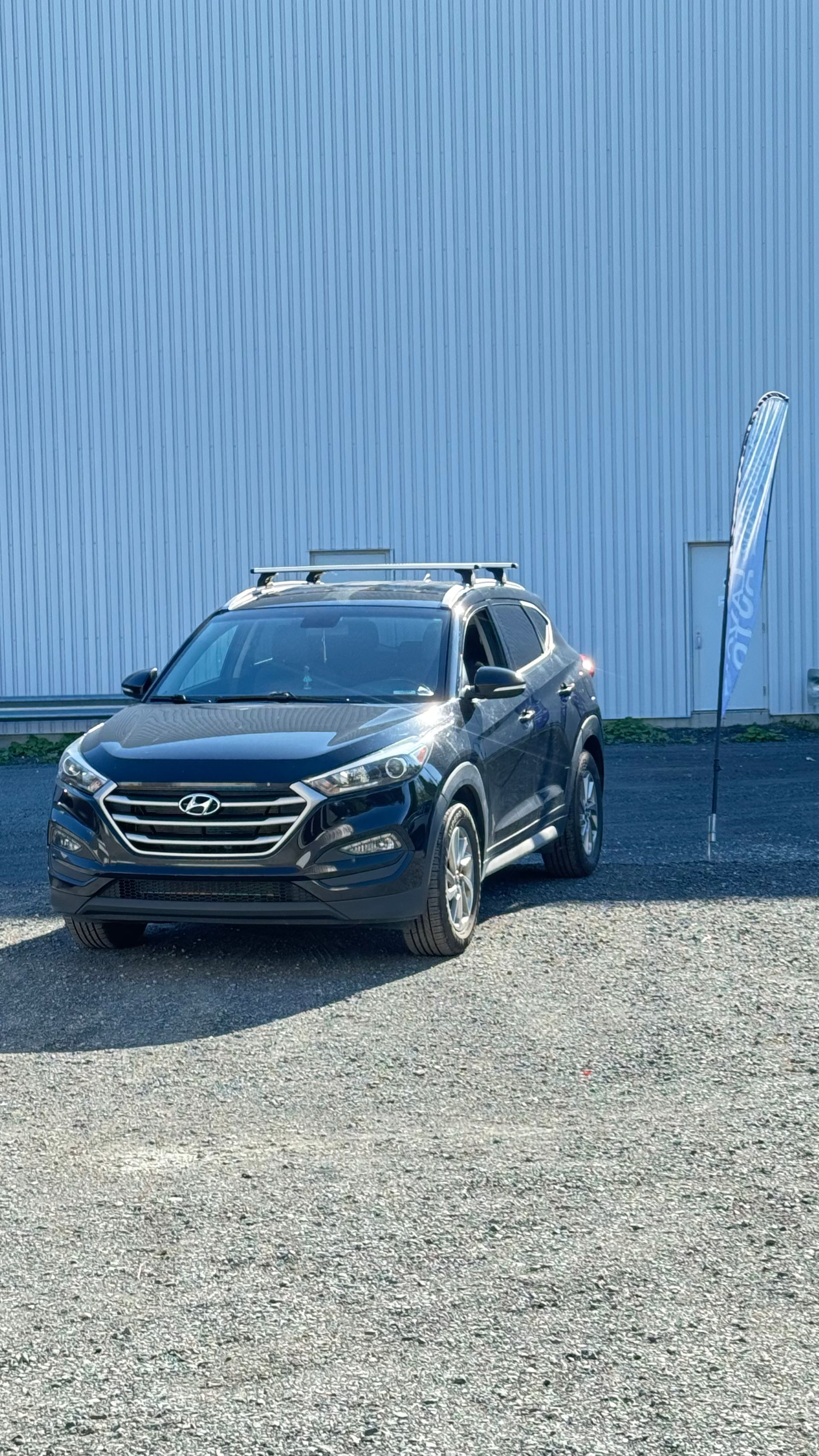 SUV Hyundai bleu foncé garé devant un bâtiment bleu, sur un terrain en gravier.